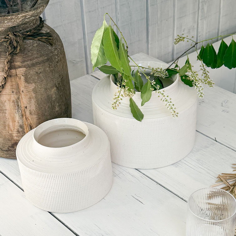 Witte matte keramische vazen op houten tafel met groene bladeren en witte bloemen
