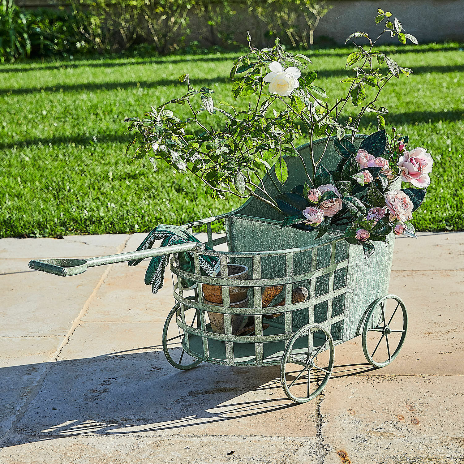 Groene metalen tuinkar met rozen en potten op terras, tuingereedschap