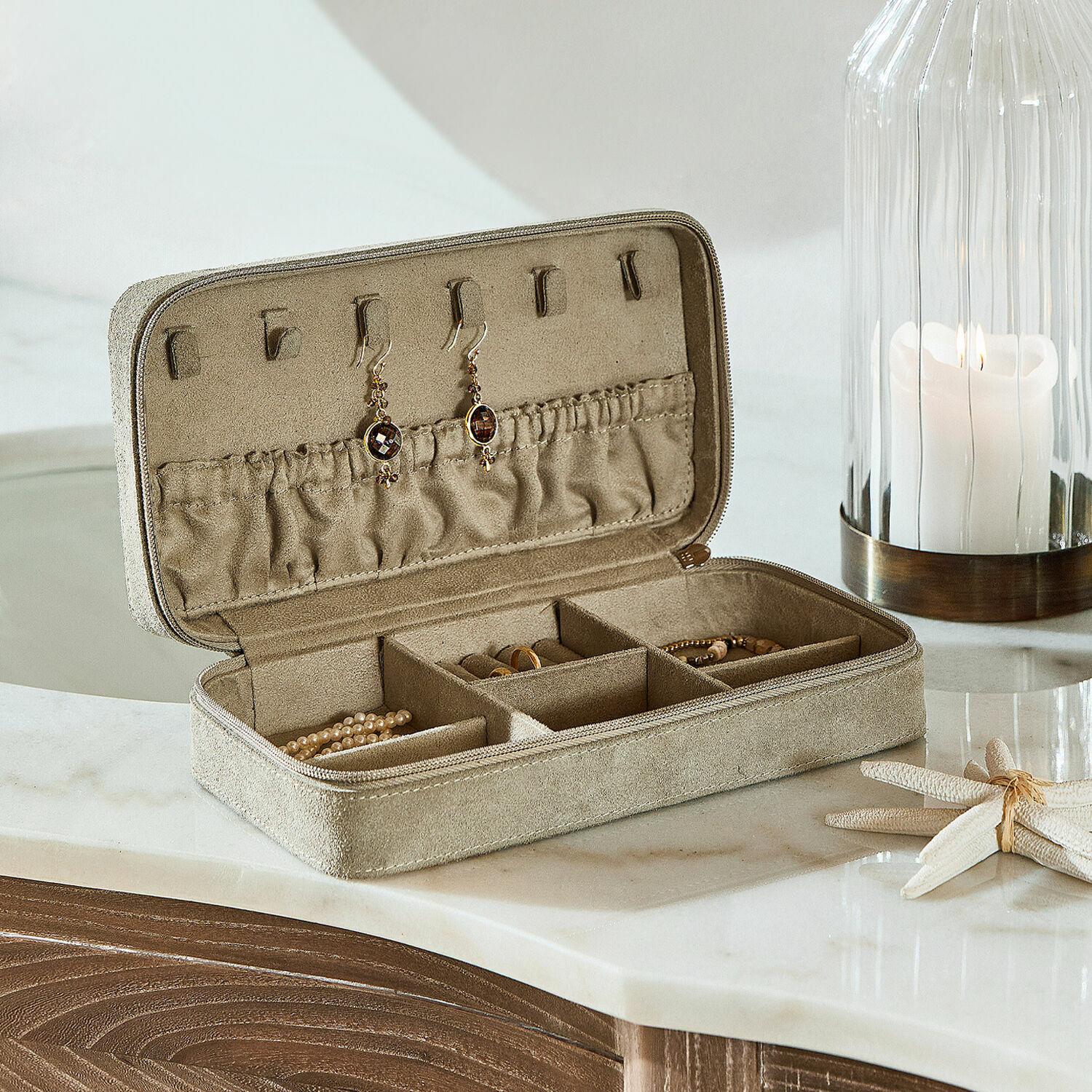 Beige suède sieradendoos met vakjes en oorbelhaken op een marmeren blad