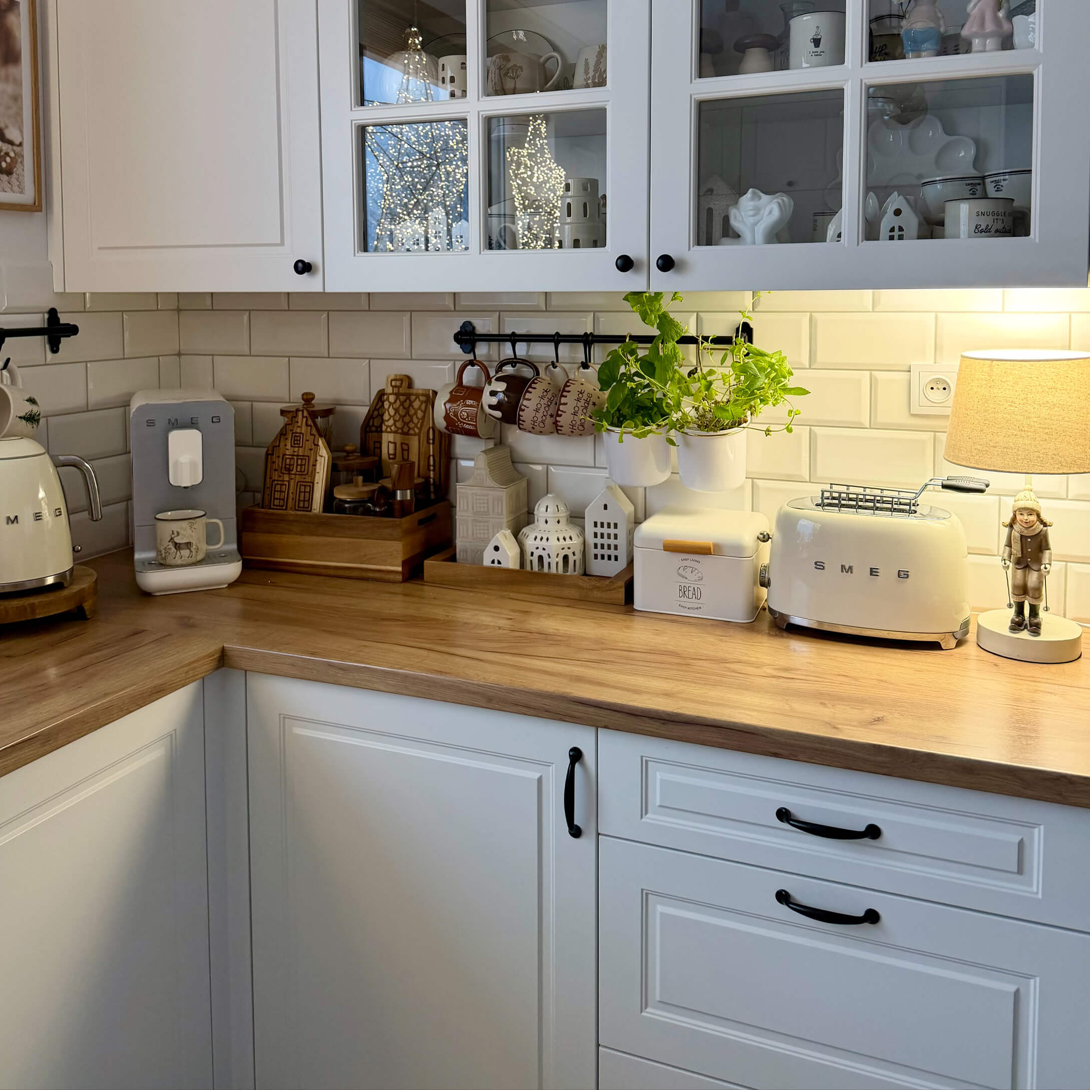 Keuken met witte kasten, houten werkblad, crèmekleurige SMEG-apparaten en decoraties met groene planten