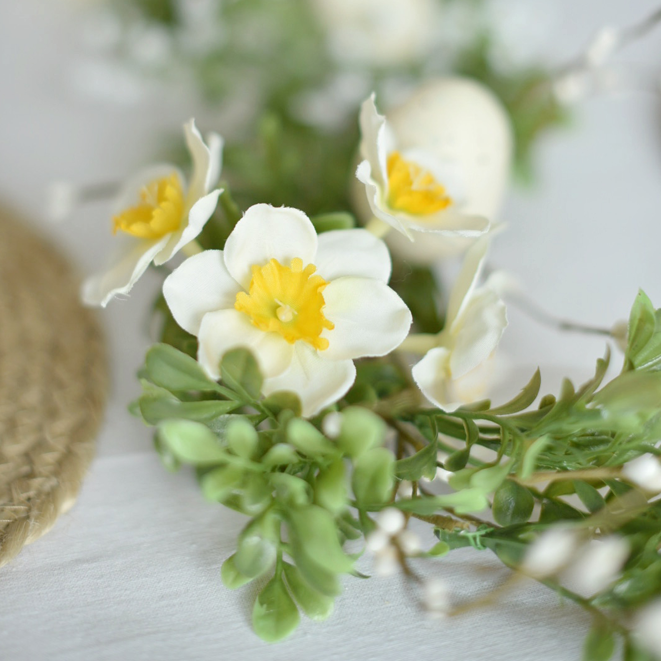 Decoratieve krans met witte en gele bloemen en groene bladeren op een lichte achtergrond