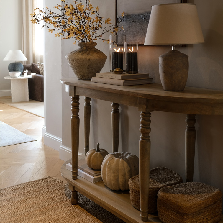 Houten sidetable met herfstdecoratie, lamp en kaarsen in een gezellige woonkamer met natuurlijke accenten