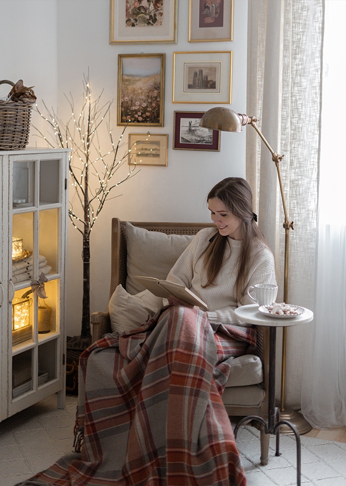 Vrouw leest boek onder warme deken in gezellige woonkamer met lamp en wanddecoraties