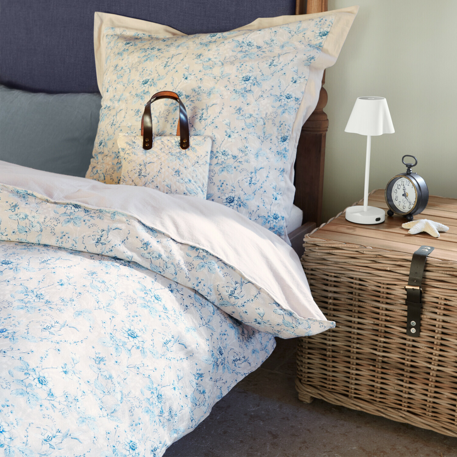 Katoenen beddengoed met lichtblauwe bloemen op bed naast rieten kastje en lamp