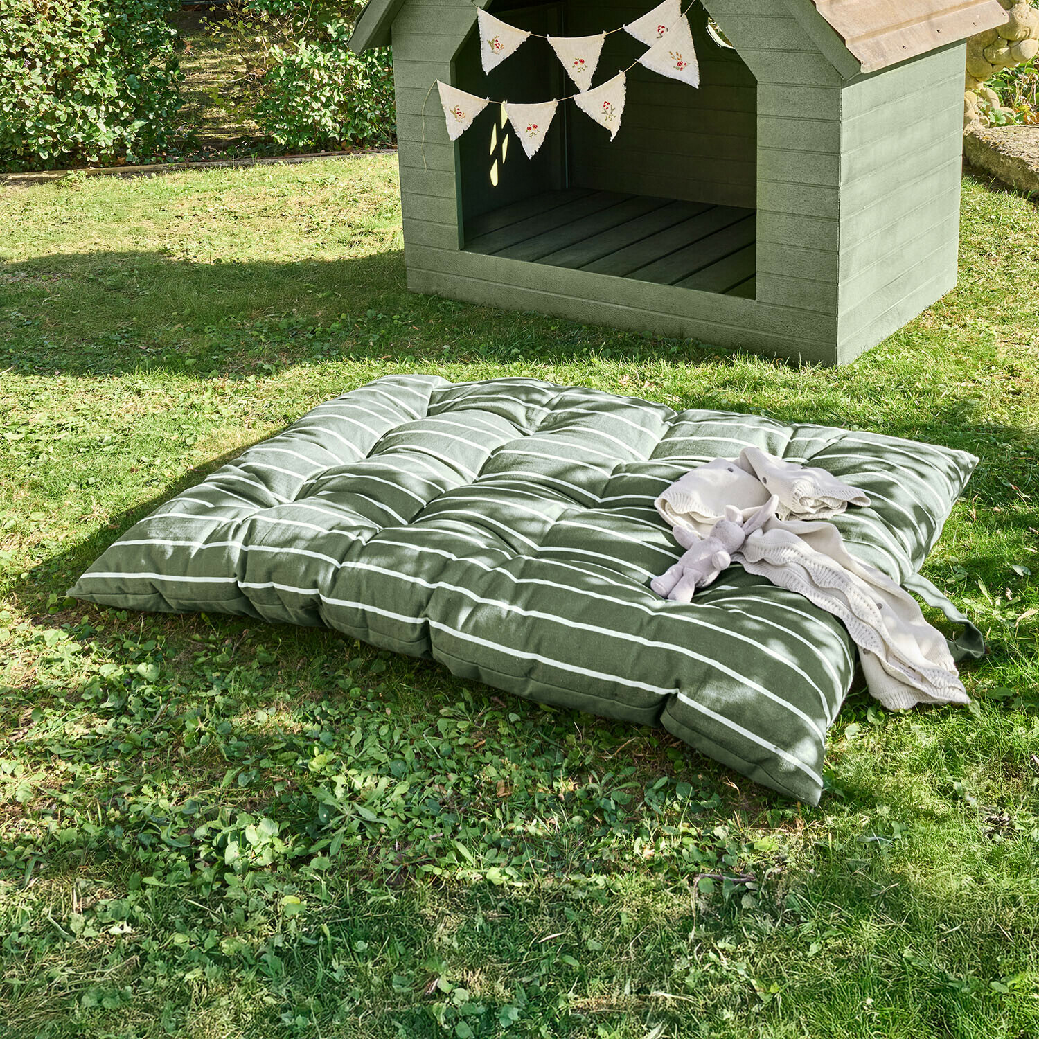 Zachte groene gestreepte kussen op gras naast houten hondenhok met decoratieve vlaggenlijn