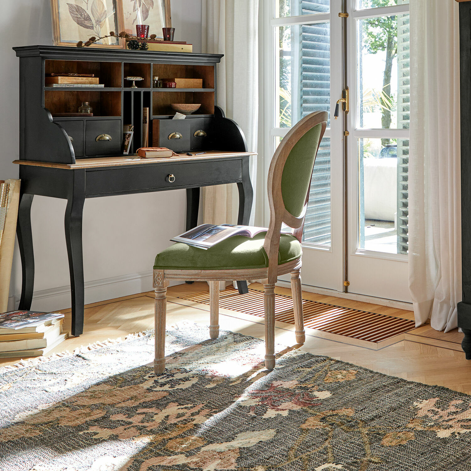 Klassiek zwart houten bureau met vakken en groen gestoffeerde stoel in lichte kamer
