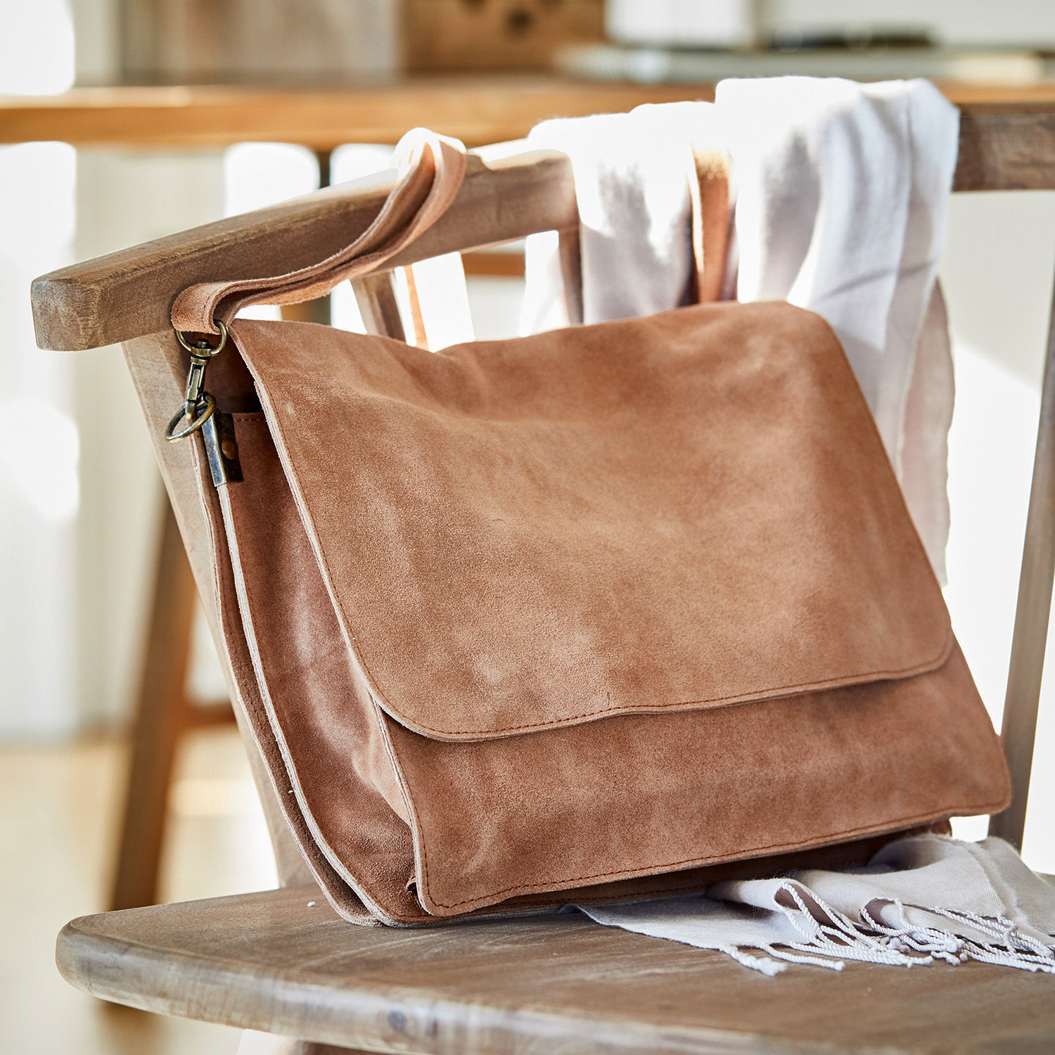 Tas Chanzelle Bruine suède schoudertas op een houten stoel, modieuze accessoire voor dagelijks gebruik