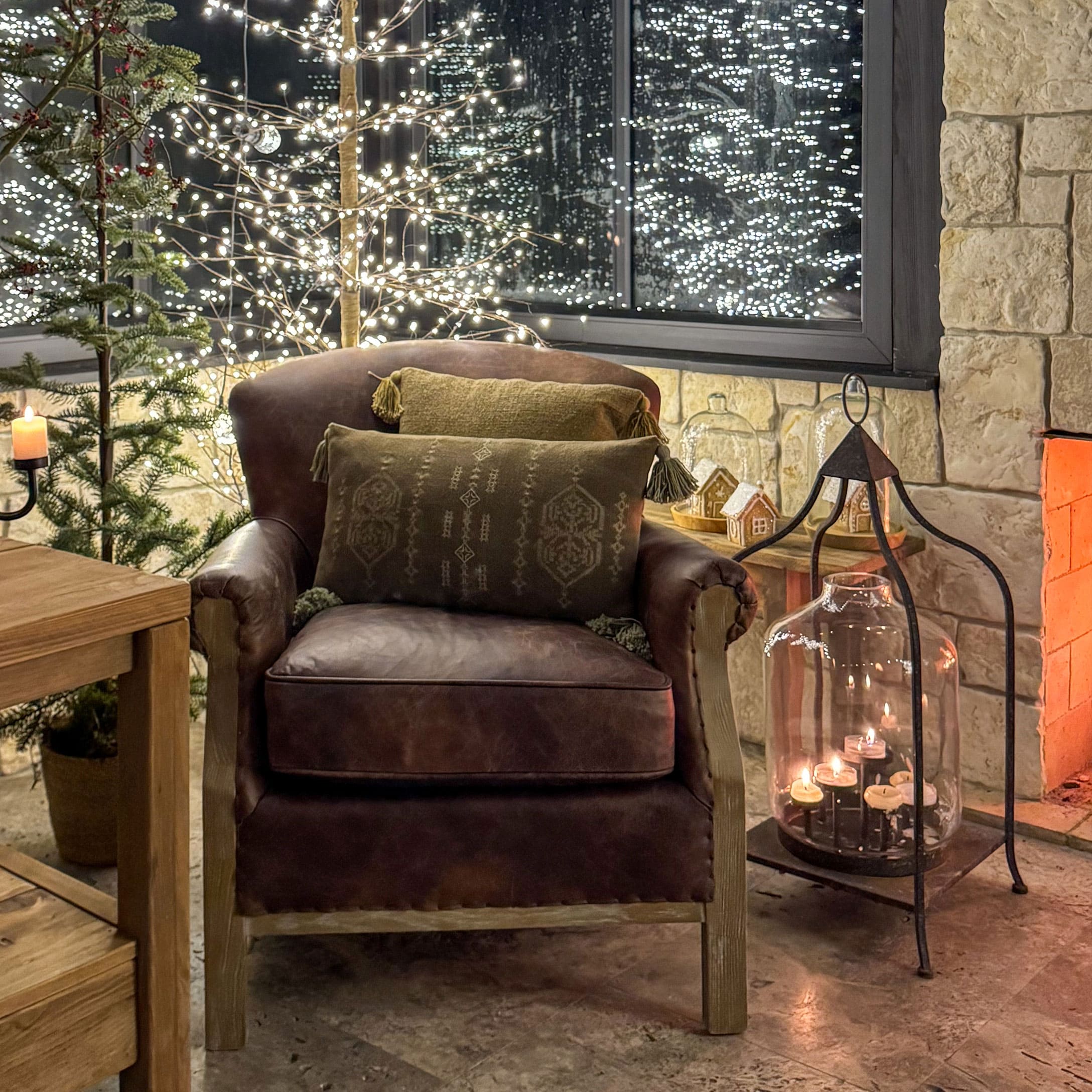 Bruine leren fauteuil met groene kussens bij kerstverlichting en brandende open haard