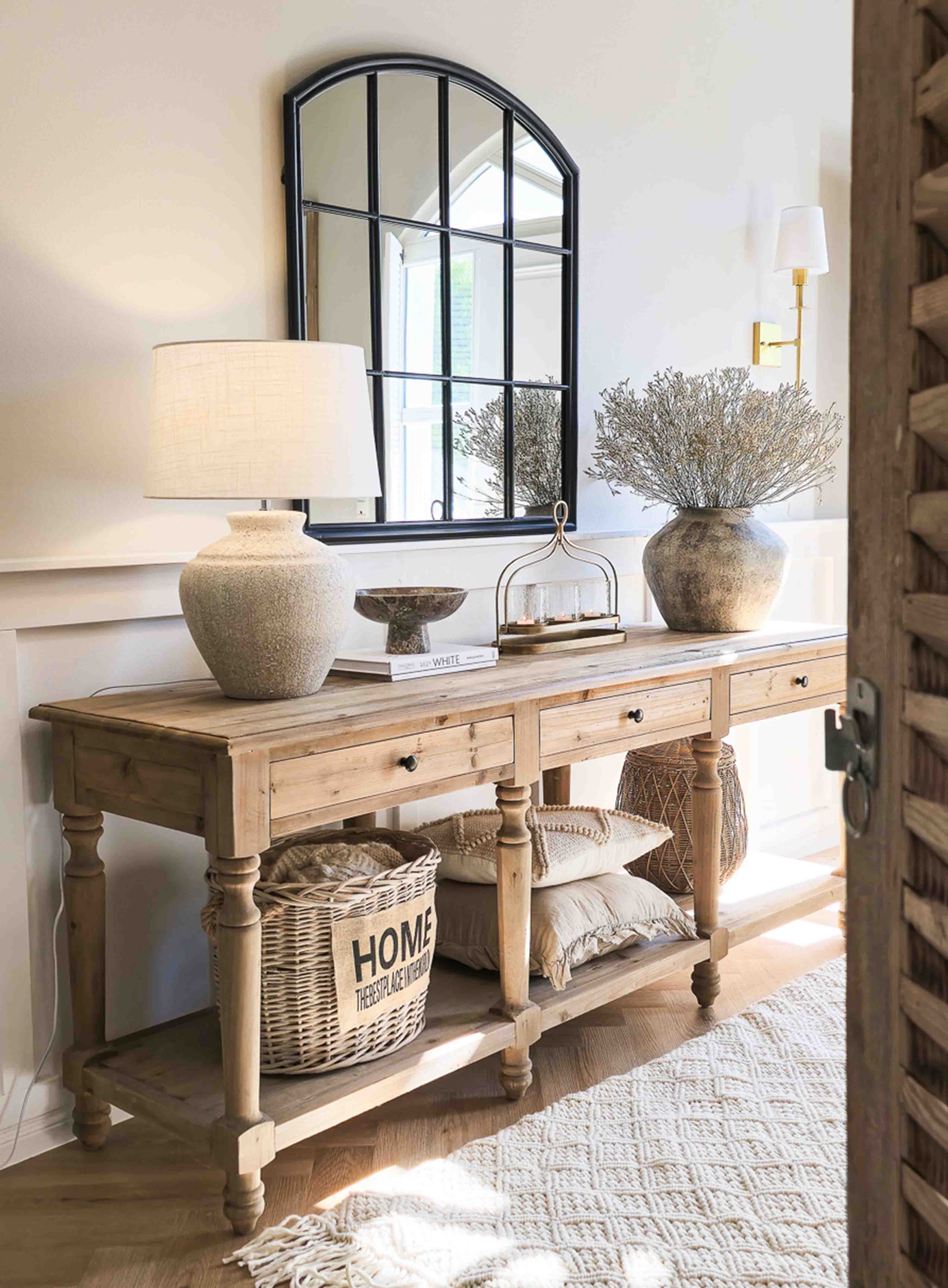 Houten sidetable met keramische lamp, zwarte lijstspiegel en rustieke decoratie in lichte kamer