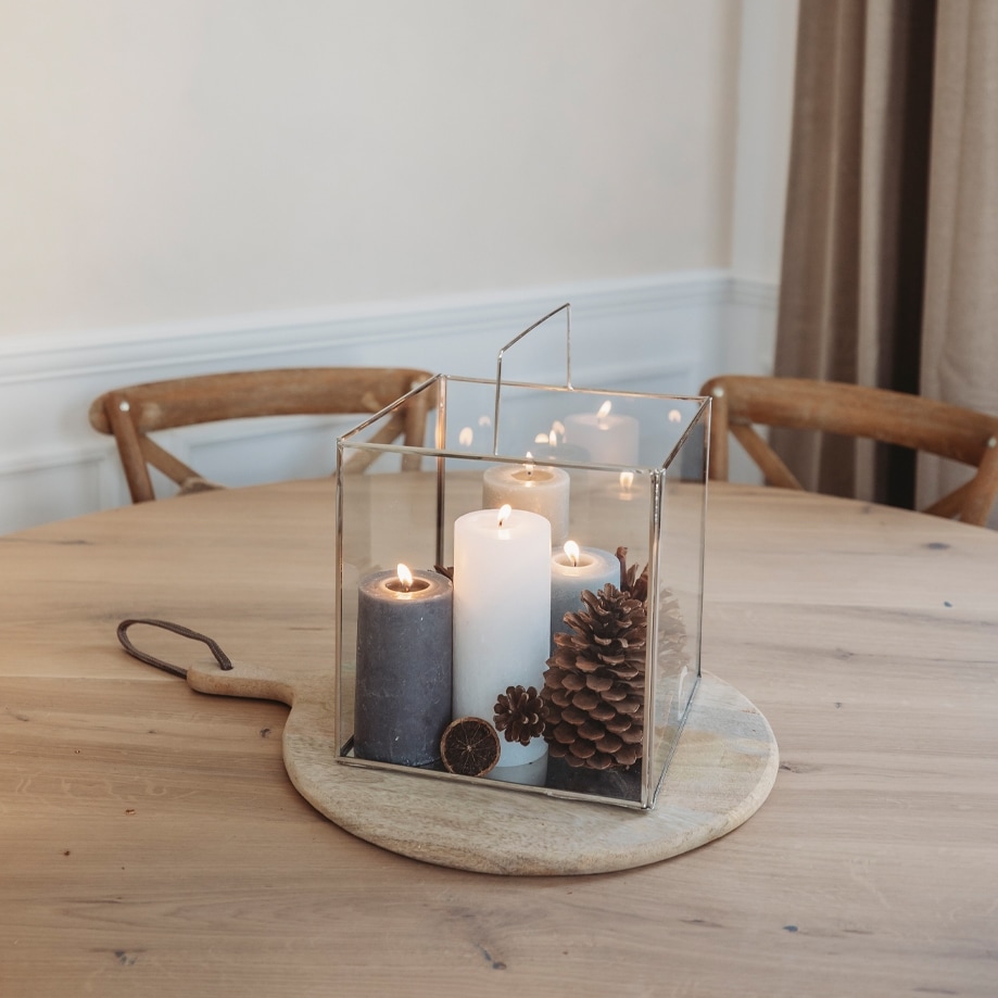 Glazen lantaarn met drie kaarsen en dennenappels op houten plank, kerstdecoratie op tafel
