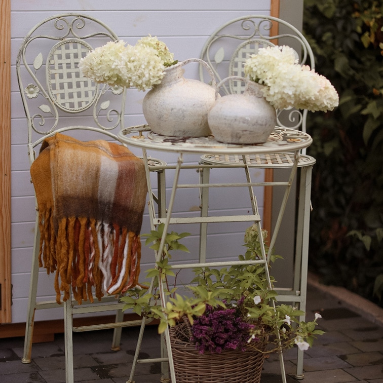 Lichtgekleurde metalen vintage tafel en twee stoelen met decoratieve witte vazen en bloemen