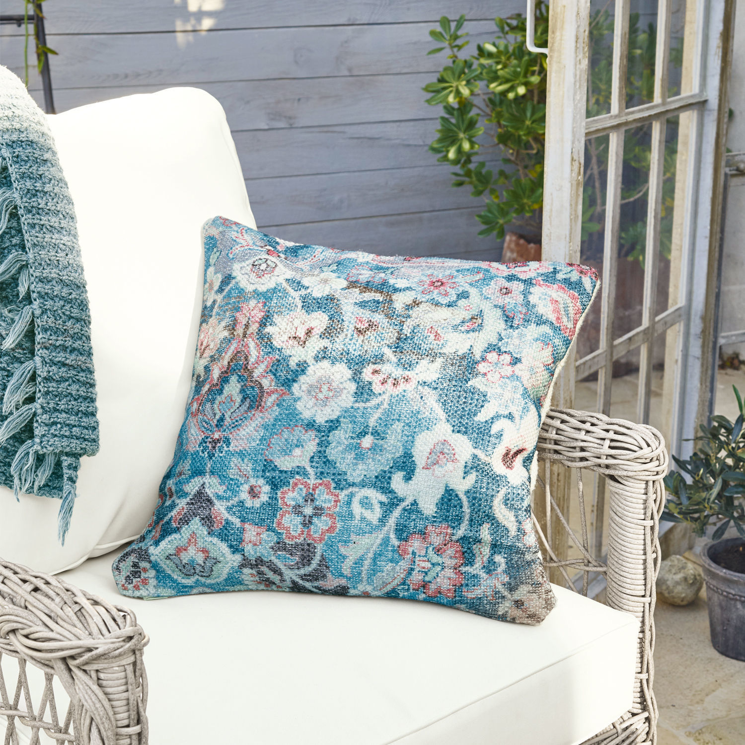 Decoratief kussen van stof met blauw-roze bloemenpatroon op witte rotan stoel