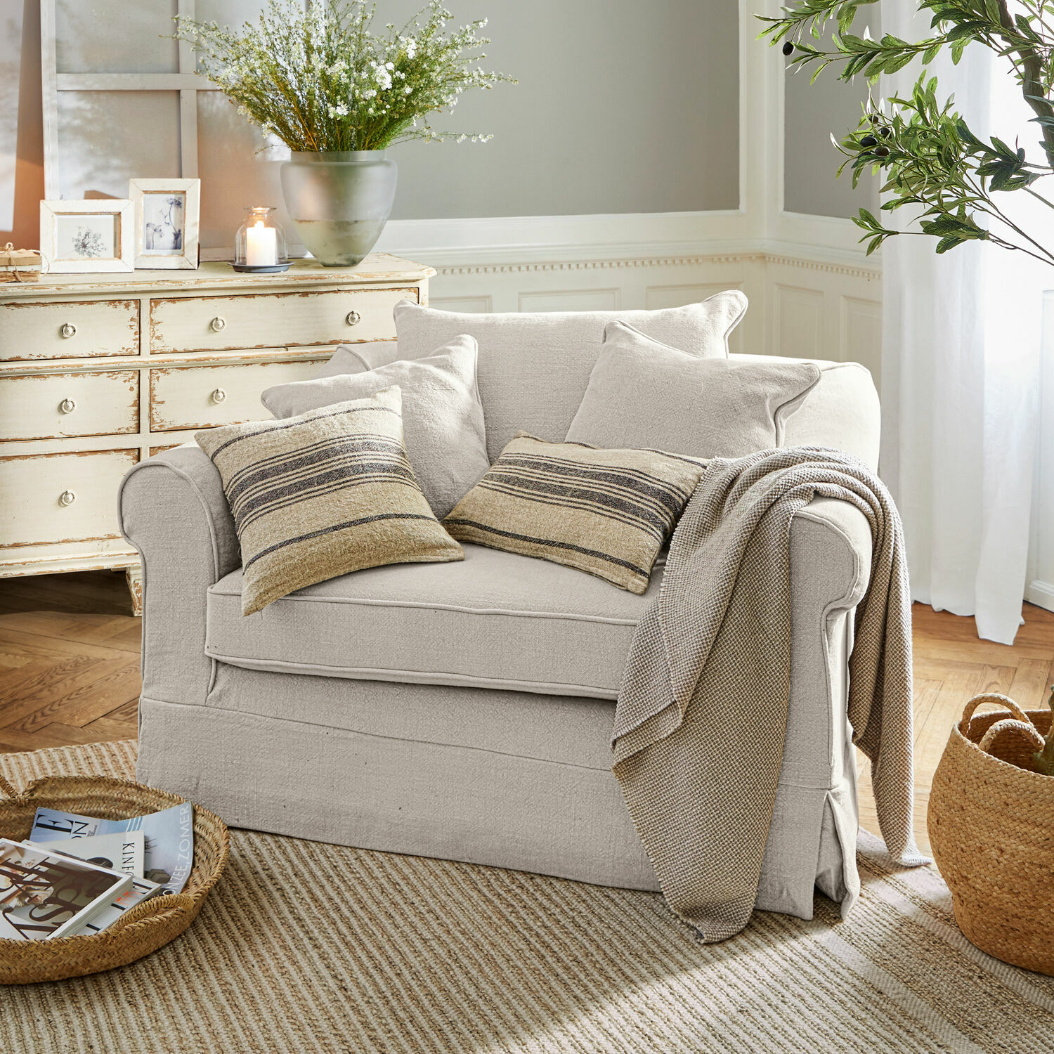 Beige stoffen bank met gestreepte kussens en deken in gezellige woonkamer met natuurlijke vloerkleed