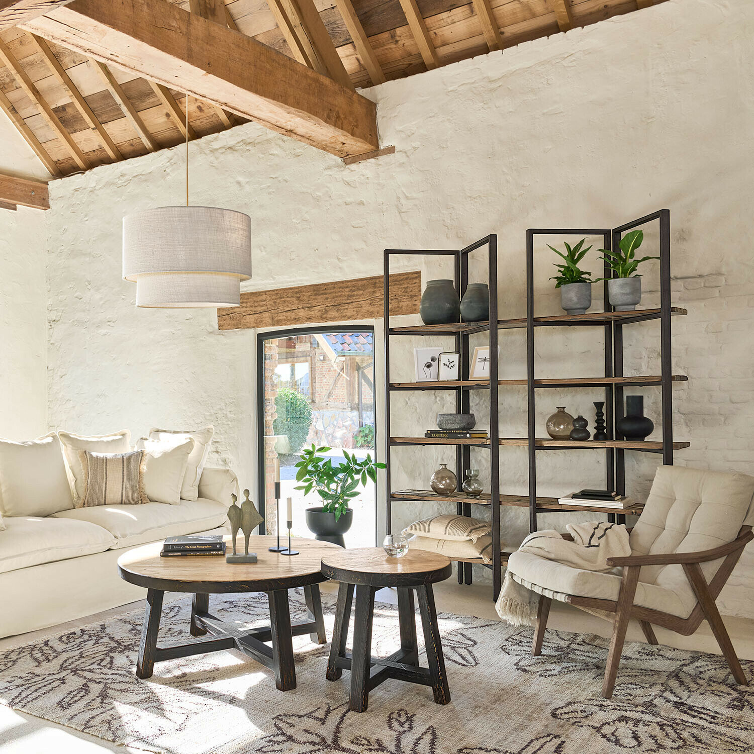 Gezellige woonkamer met houten tafels, crèmekleurige bank en metalen kast met decoraties