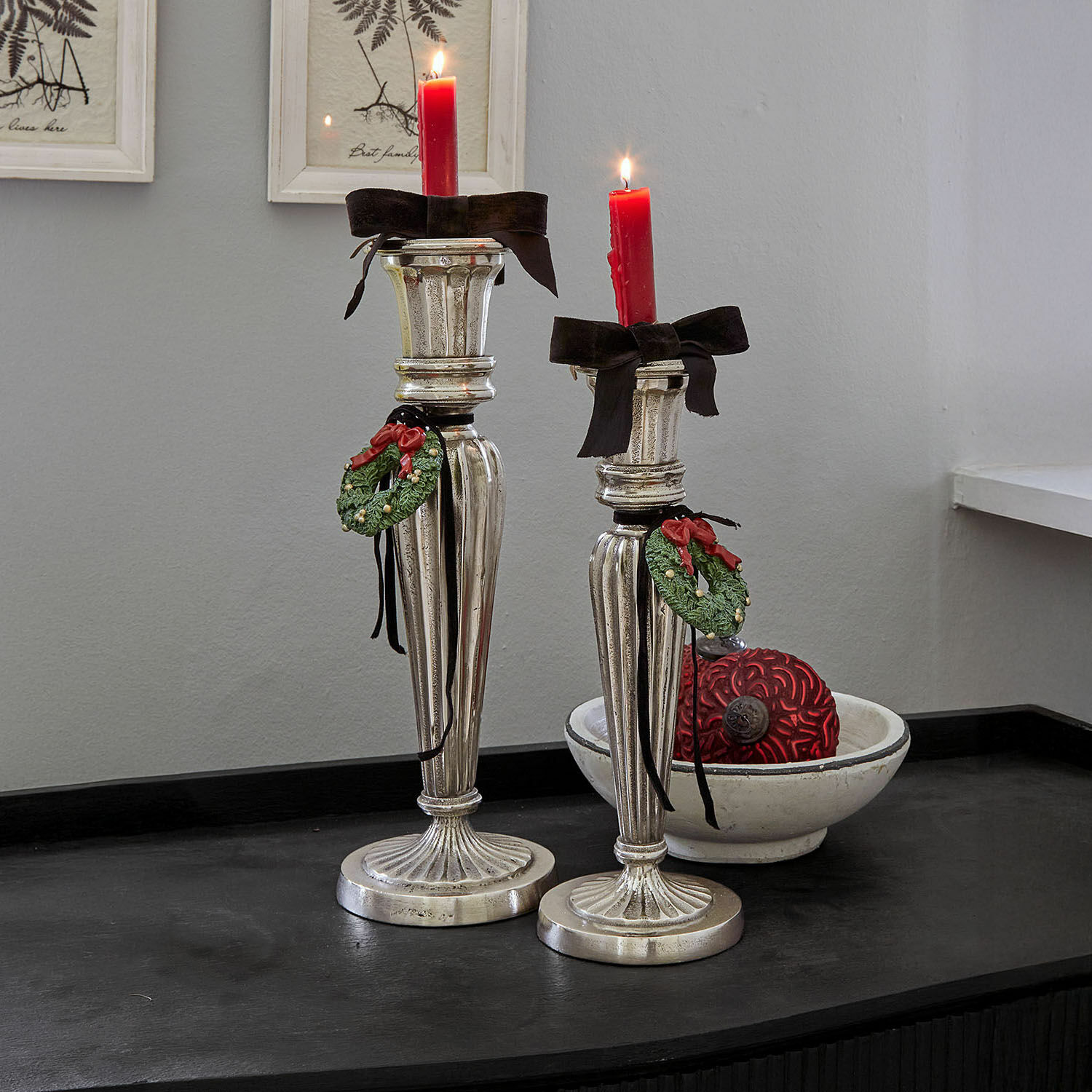 Twee zilveren kandelaars met rode kaarsen en groene kransdecoraties op zwart oppervlak