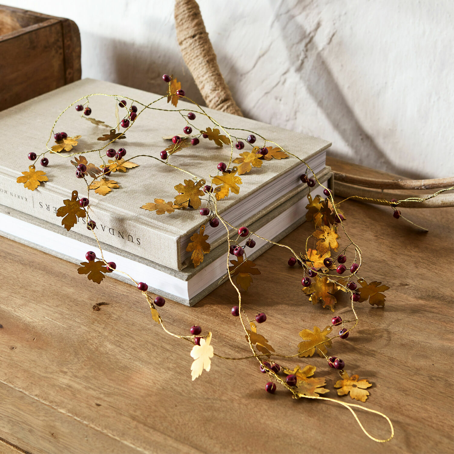 Guirlande Liezel Decoratieve slinger met gouden metalen bladeren en rode bessen op houten tafel