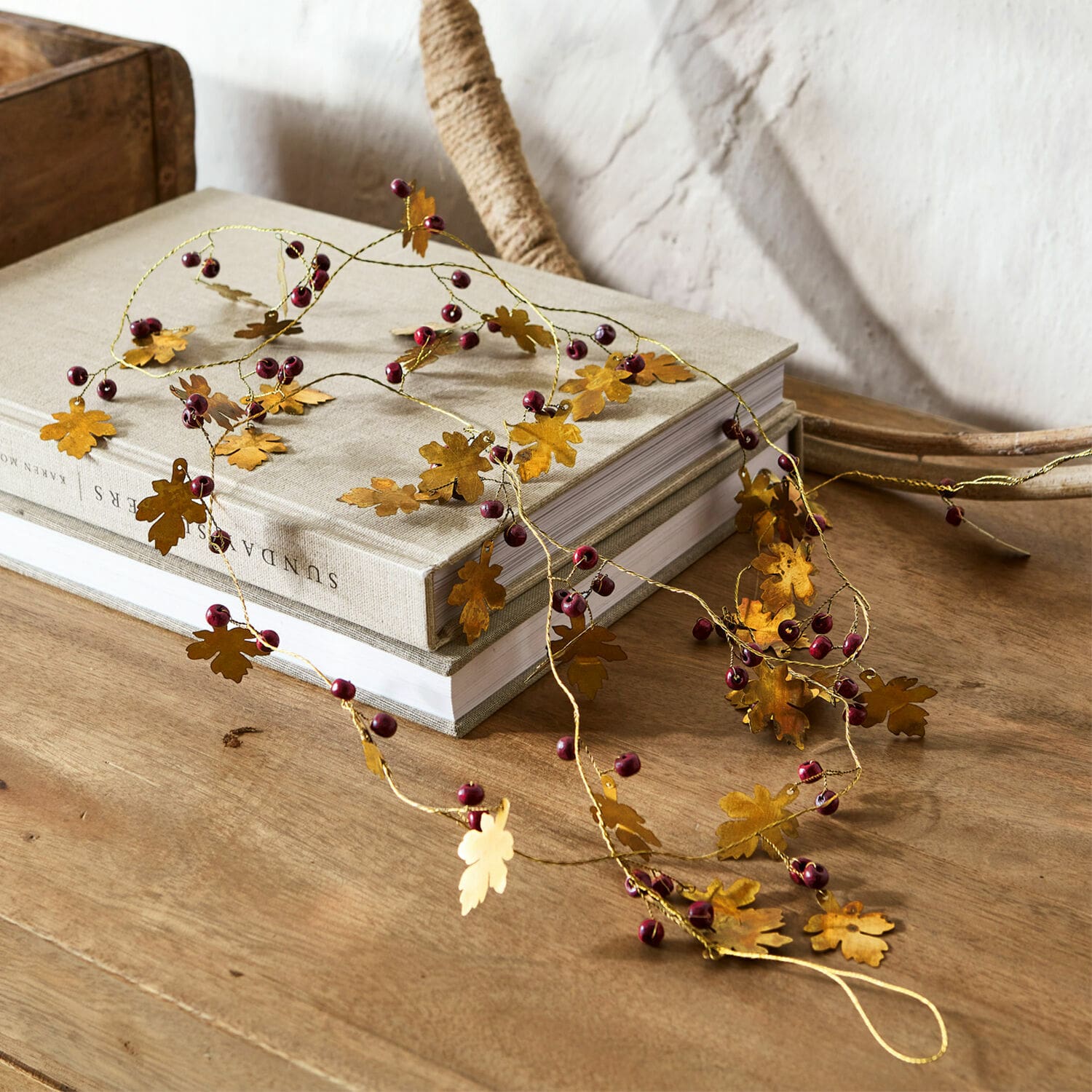 Guirlande Liezel Decoratieve slinger met gouden metalen bladeren en rode bessen op houten tafel