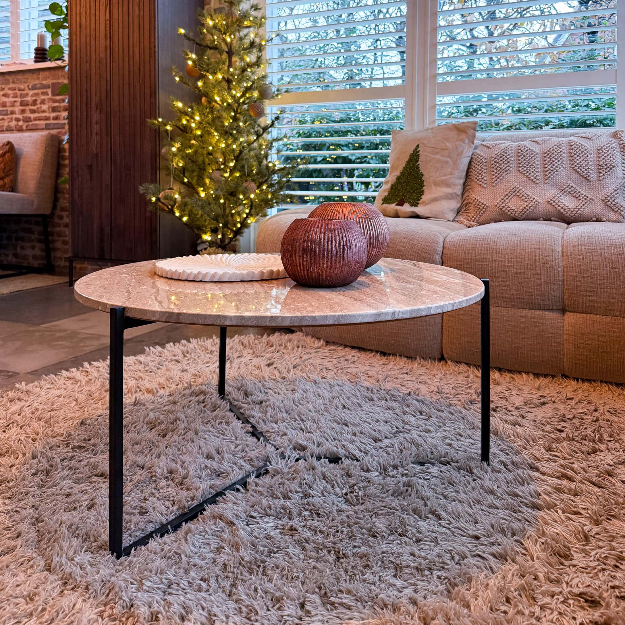 Ronde salontafel met marmeren blad en zwart metalen onderstel op een zacht vloerkleed in woonkamer