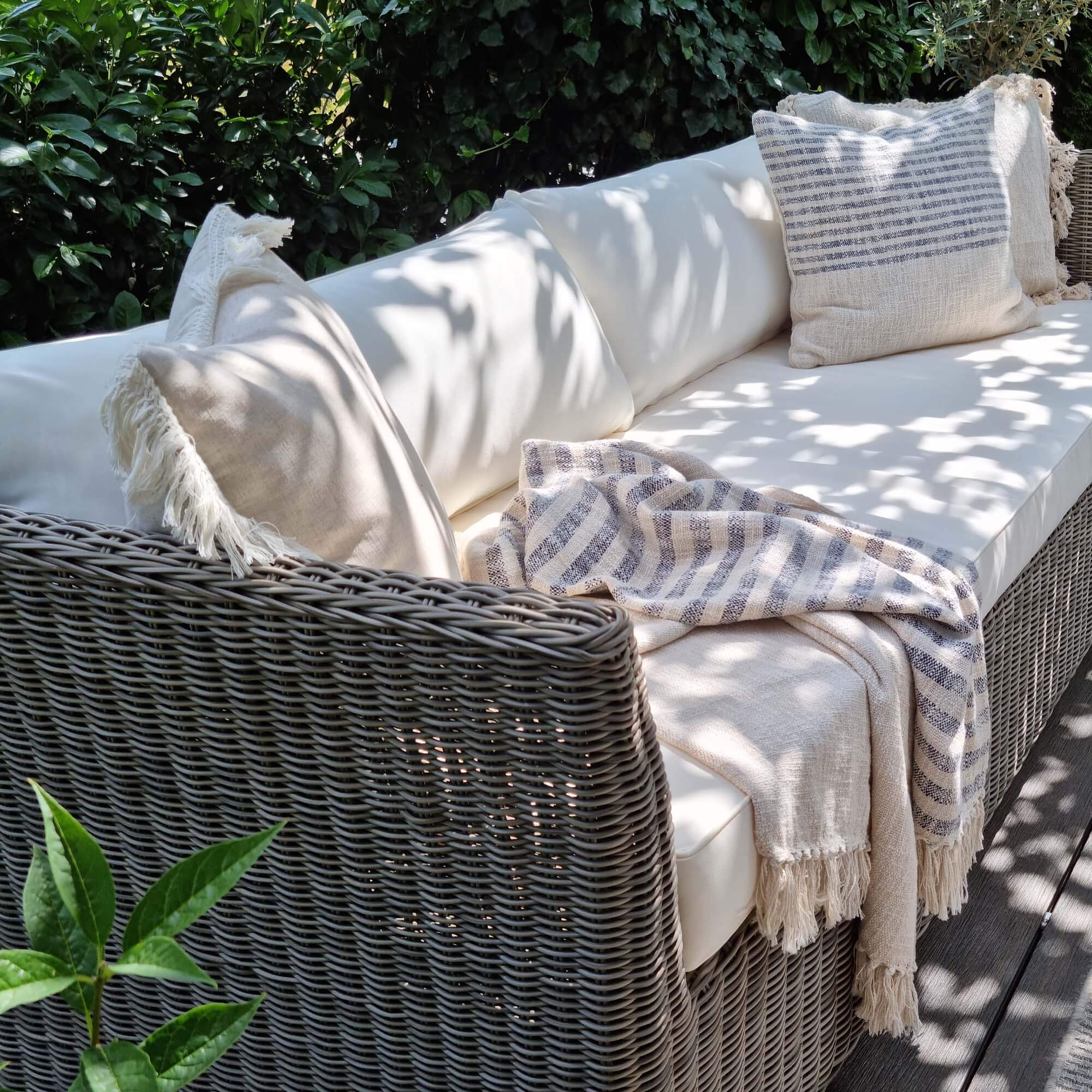 Tuinbank van grijs rattan met crèmekleurige kussens en beige gestreepte deken