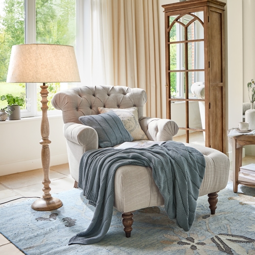 Beige Chesterfield fauteuil met houten poten en blauwe deken in lichte woonkamer