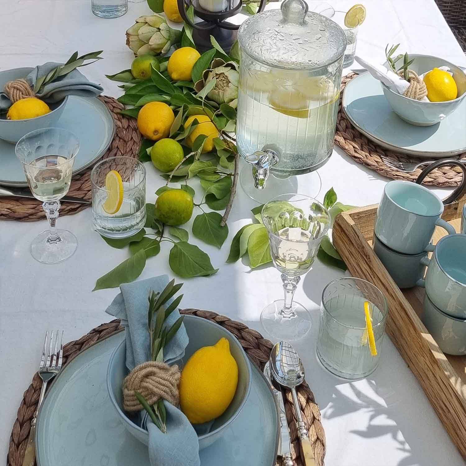 Zomerse tafel met blauw keramiek, citroenen en groene bladeren op wit tafelkleed, tafeldecoratie