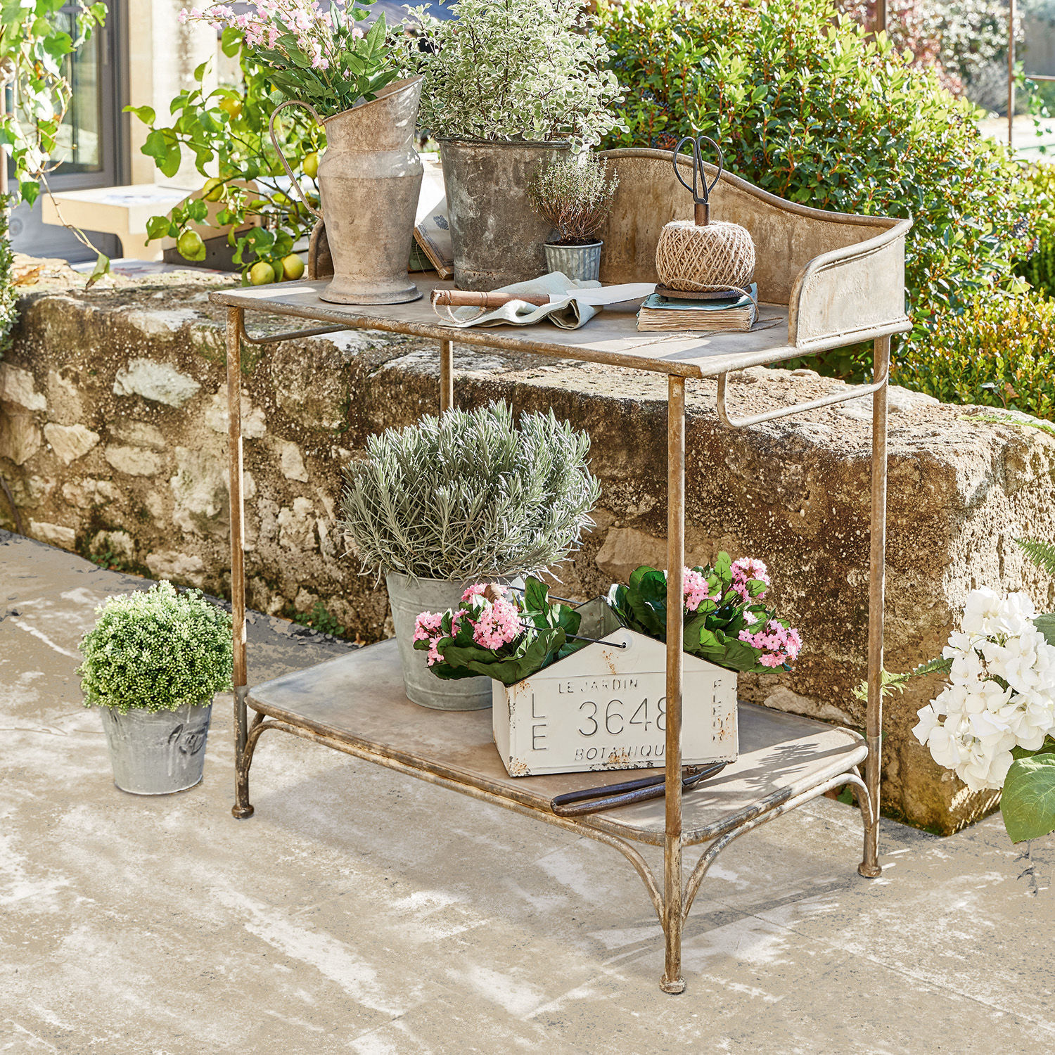 Metalen tuintafel met bloempotten en tuingereedschap voor een stenen muur