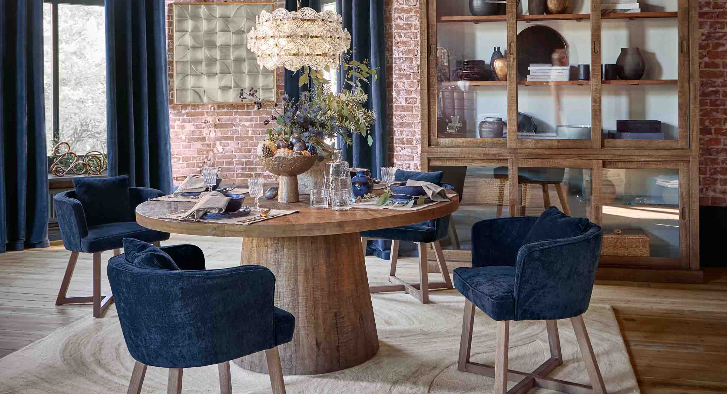 Eetkamer met ronde houten tafel en donkerblauwe fluwelen stoelen in loftstijl