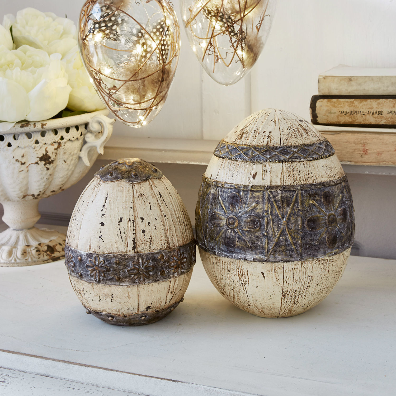 Decoratieve eieren van hout en metaal in crème met rustiek patroon op witte tafel
