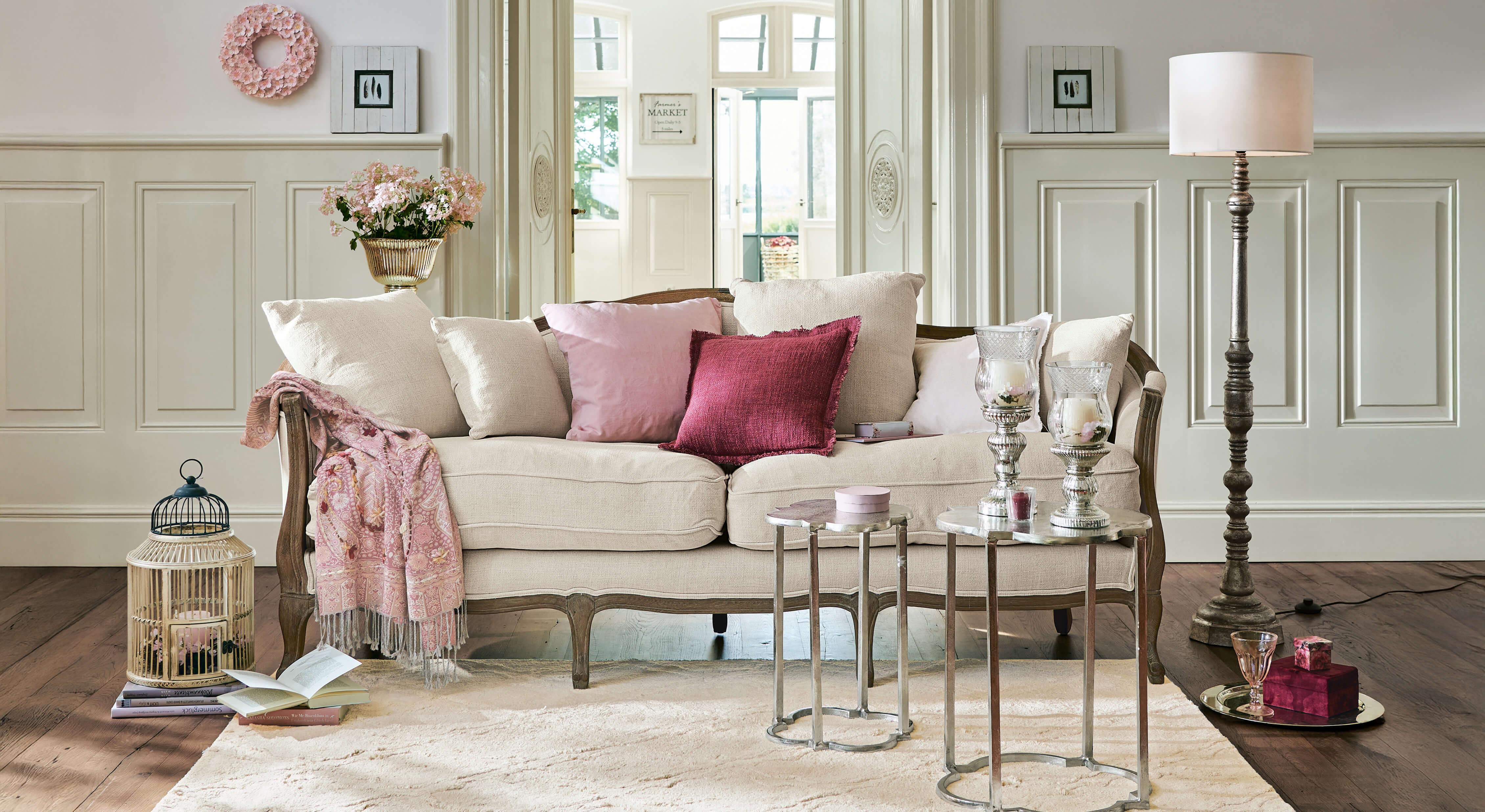 Beige bank met houten frame en roze kussens in elegante woonkamer met decoraties