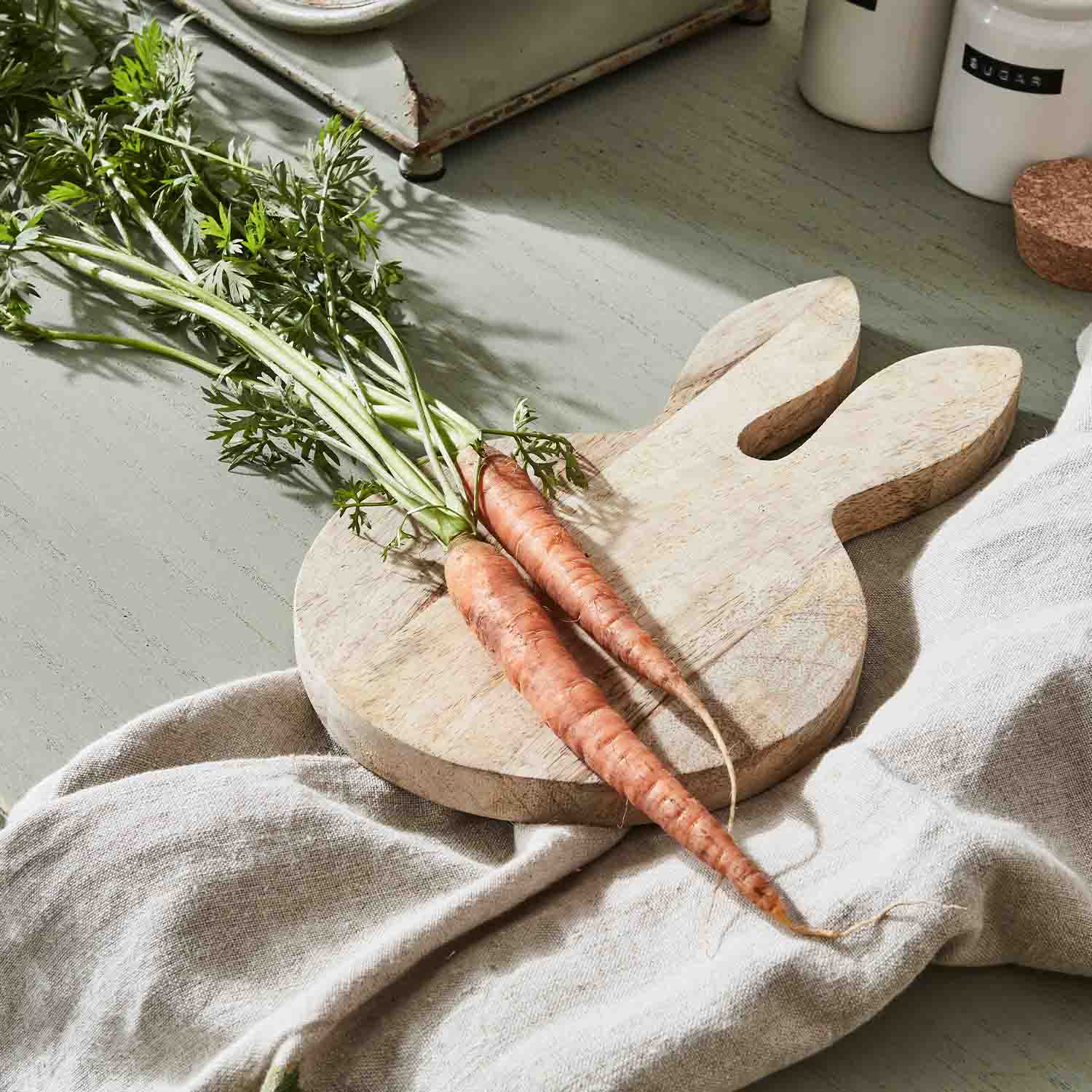 Houten snijplank in konijnenvorm met twee verse wortels op een linnen doek