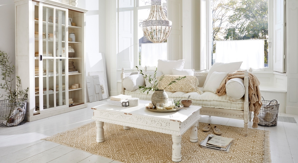 Lichte woonkamer met beige oosterse vloerkleed, witte houten salontafel en vintage bank
