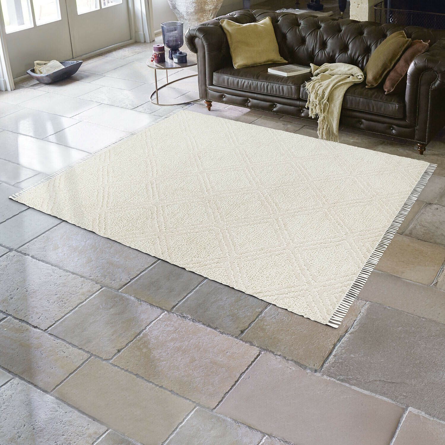 Beige vloerkleed met geometrisch patroon op stenen vloer in woonkamer met bruine leren bank