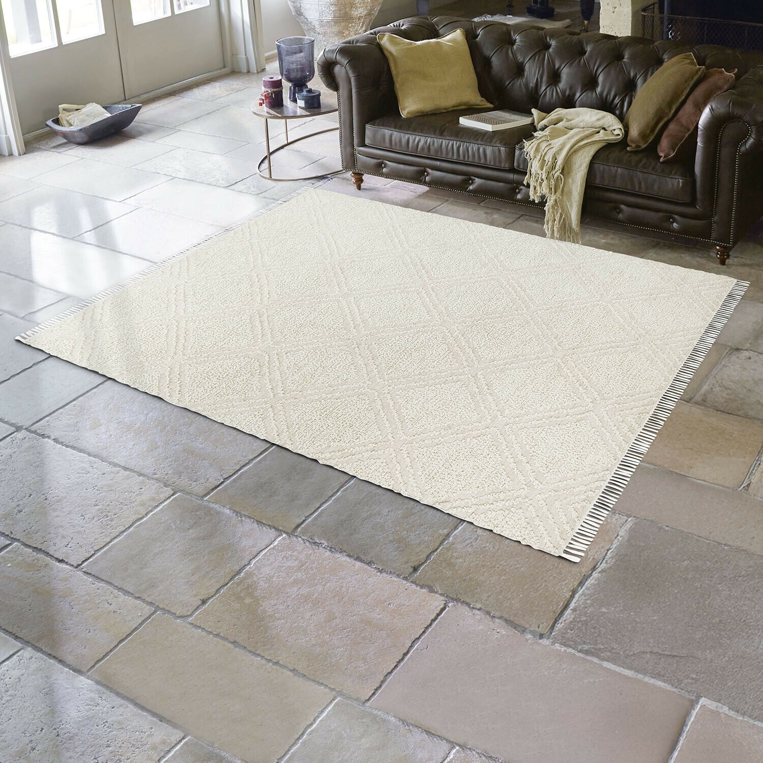 Vloerkleed voor binnen en buiten Bruand Beige vloerkleed met geometrisch patroon op stenen vloer in woonkamer met bruine leren bank