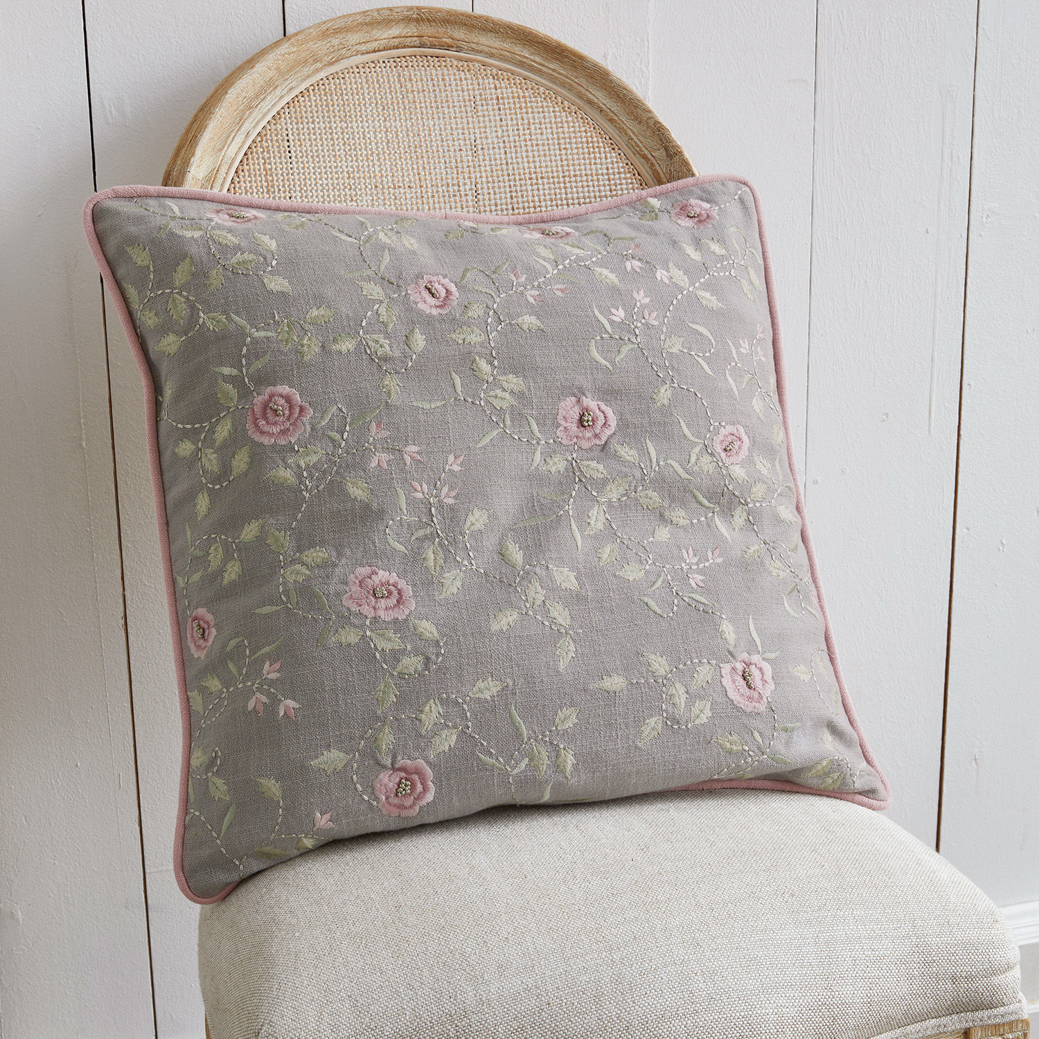 Kussen Rosalena Grijs sierkussen met roze bloemenborduursel op beige stoel, woontextiel voor gezellige ruimtes