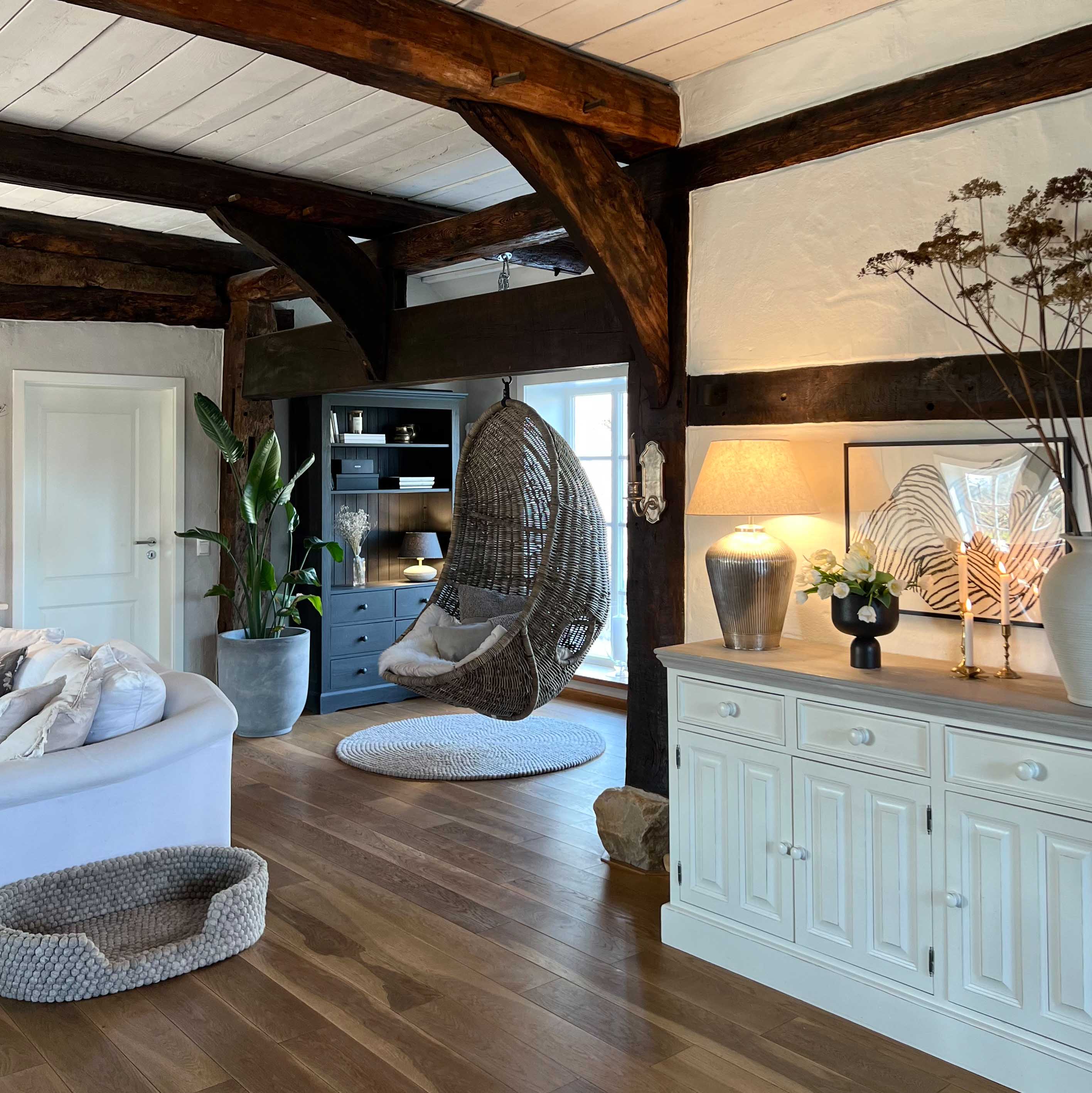 Hangstoel van grijs riet in een gezellige woonkamer met houten vloer en witte dressoir