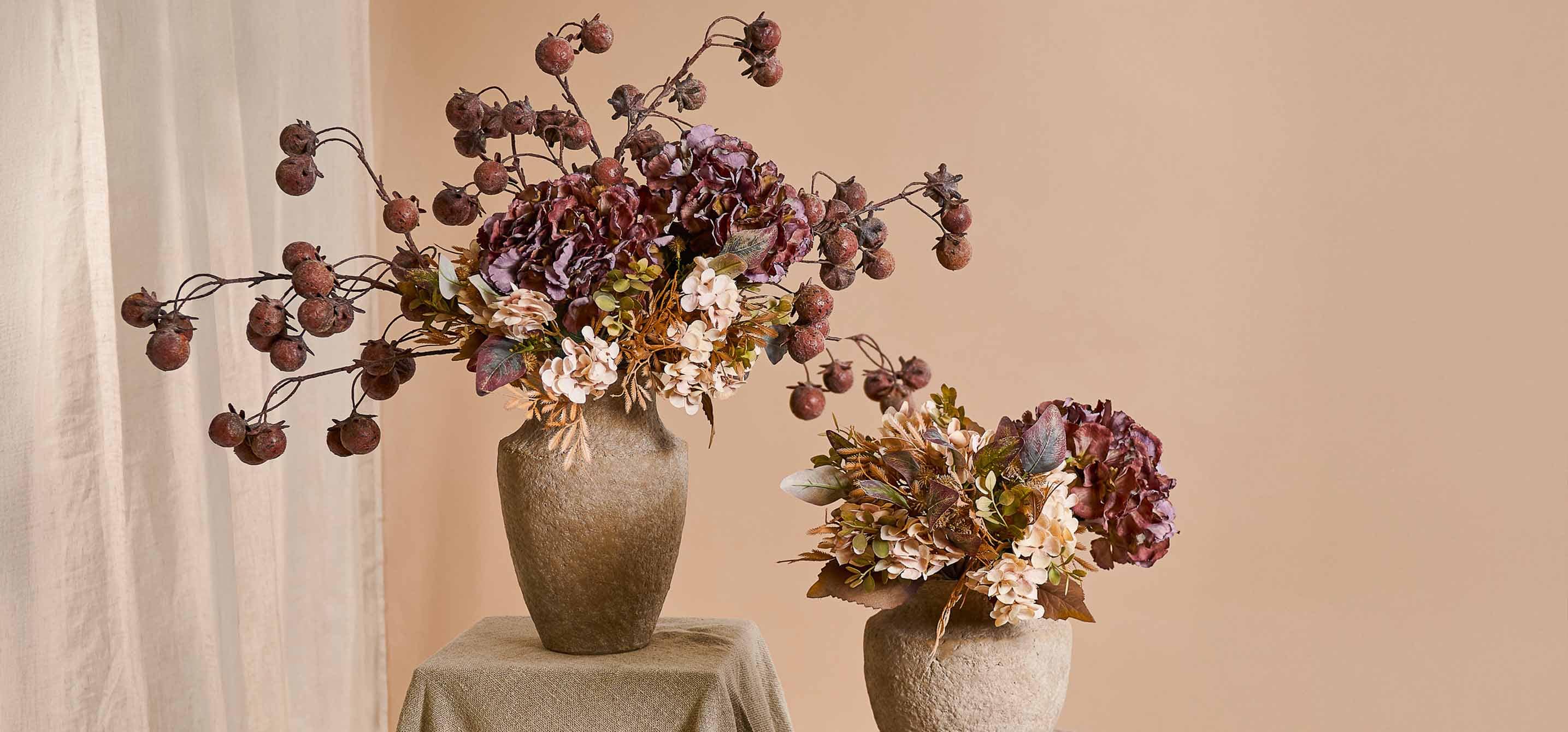 Twee decoratieve beige stenen vazen met herfstbloemen en gedroogd fruit in warme kleuren voor interieurdecoratie