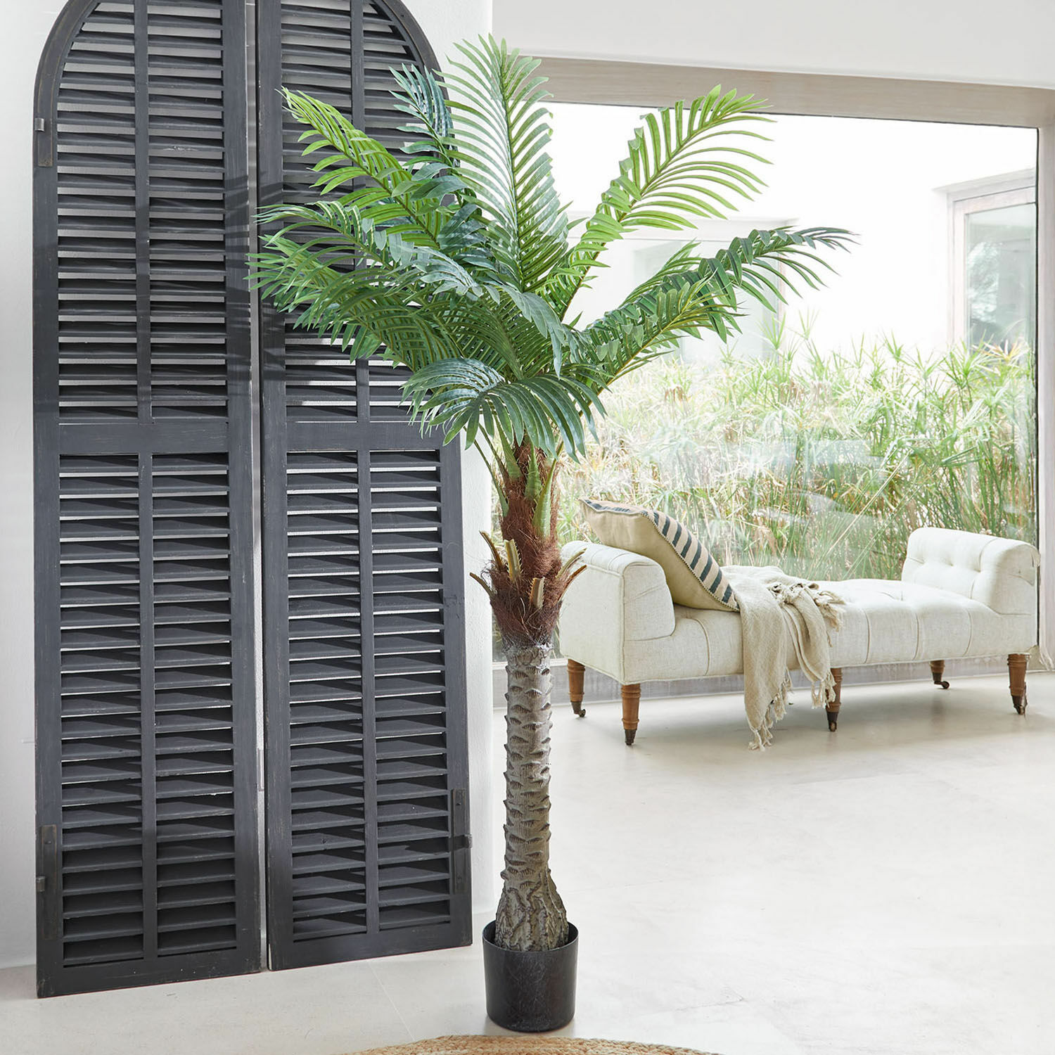 Decoratieve potplant Zephyriel Kunstpalm in zwarte pot in lichte woonkamer met beige bank en groot raam