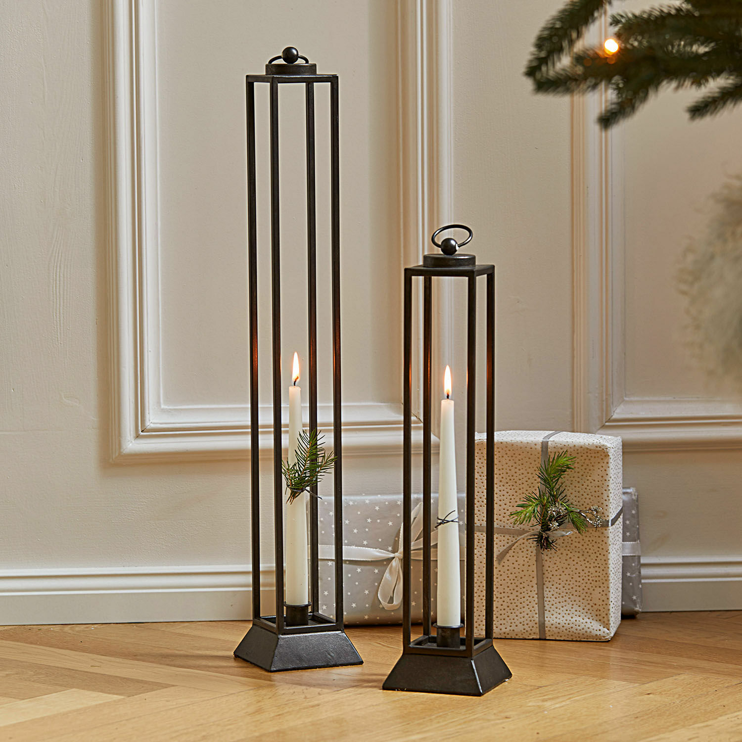 Twee zwarte metalen lantaarns met witte kaarsen en takdecoratie op houten vloer