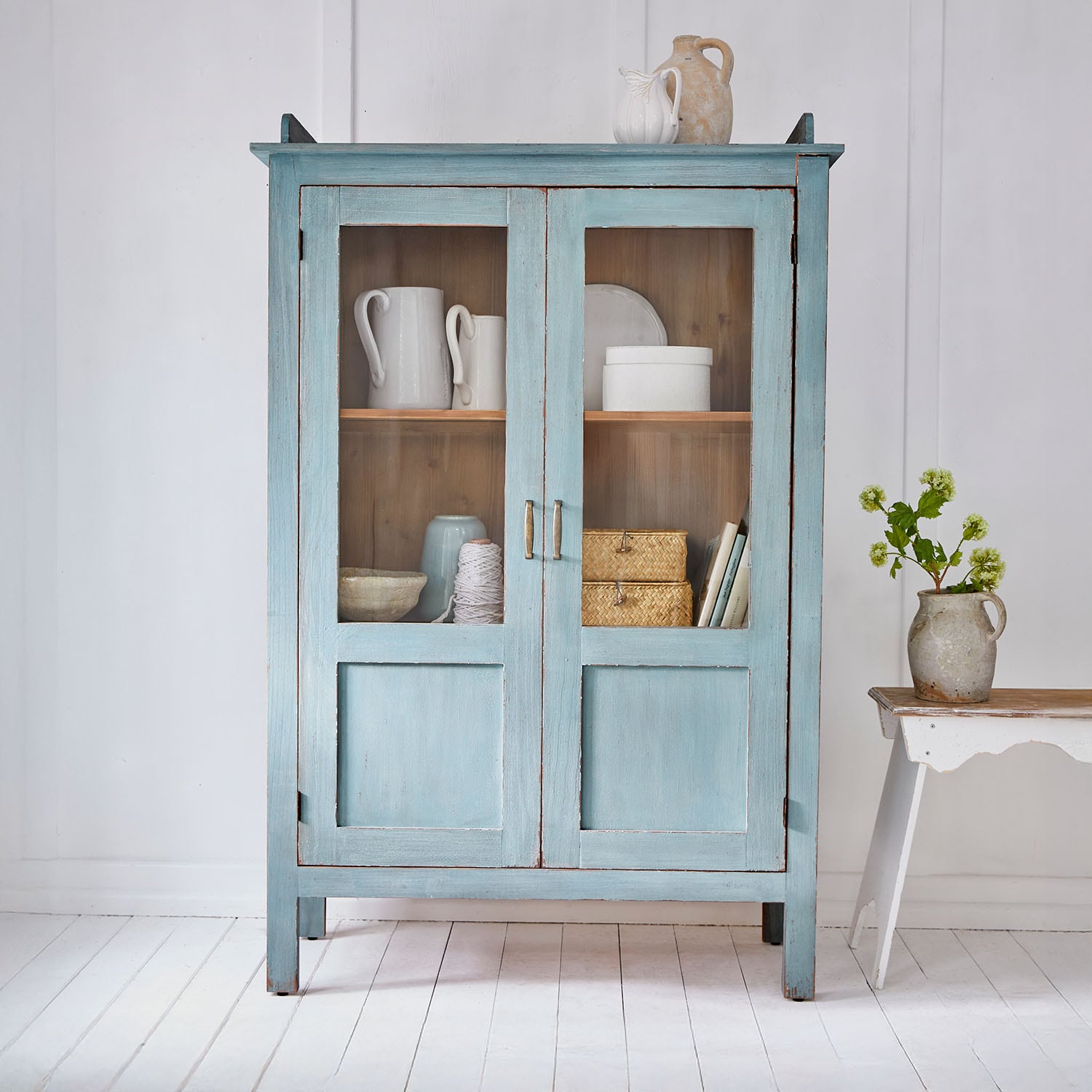Blauwe houten kast met glazen deuren en vintage keramische decoraties in lichte kamer