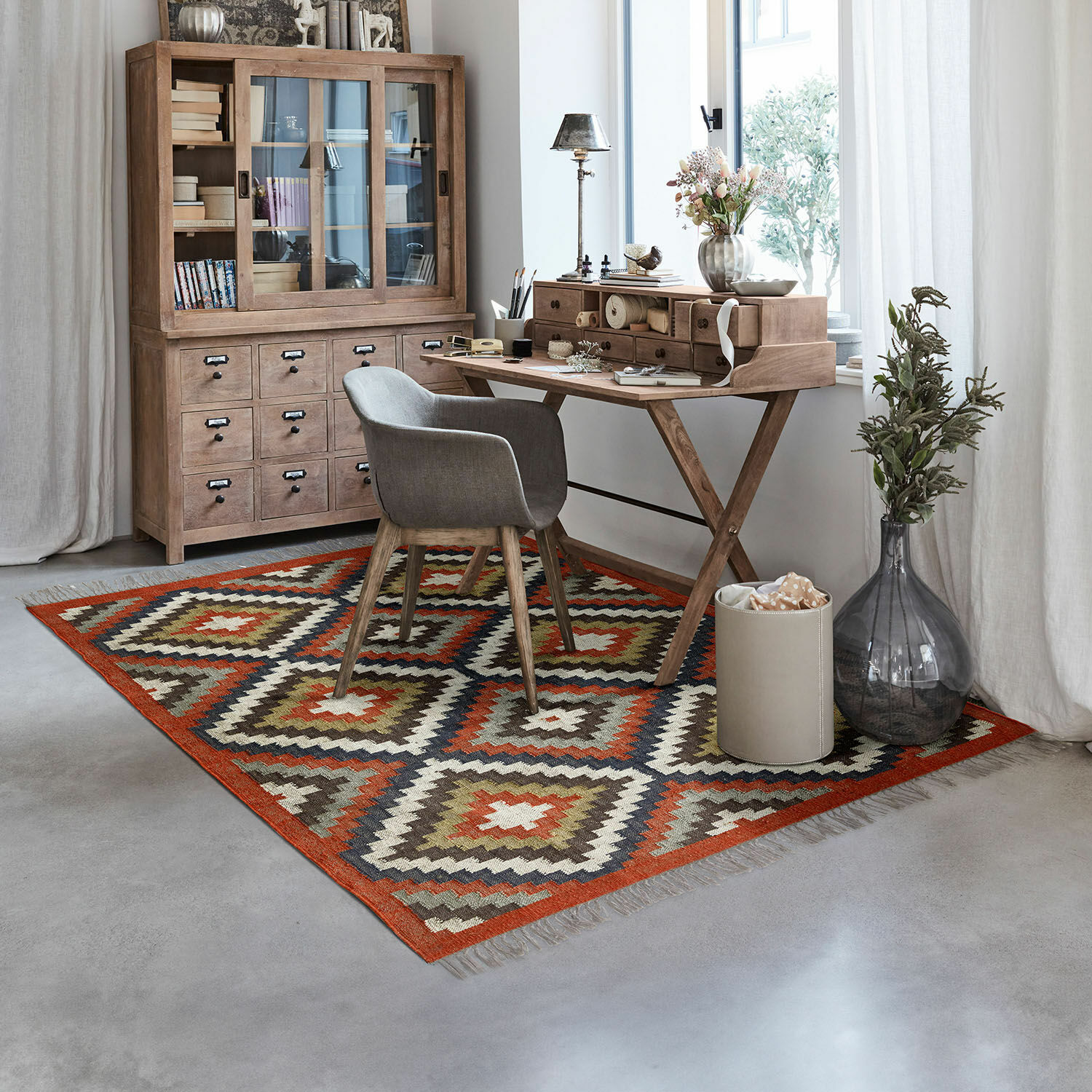 Vloerkleed met geometrisch patroon in warme kleuren in modern kantoor met houten bureau en grijze stoel