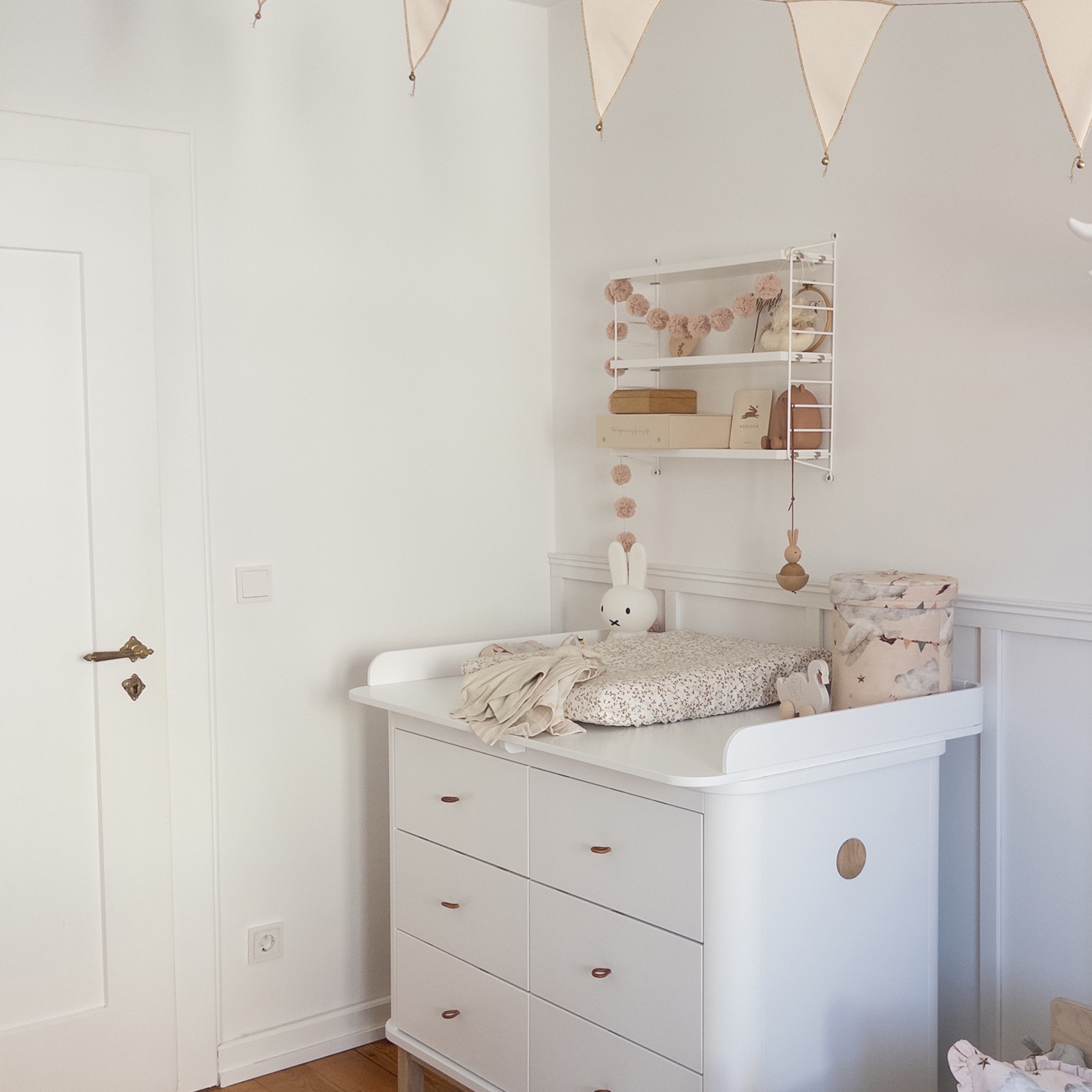 Witte kinderkast met verschoontafel en pastelkleurige decoraties in lichte kinderkamer