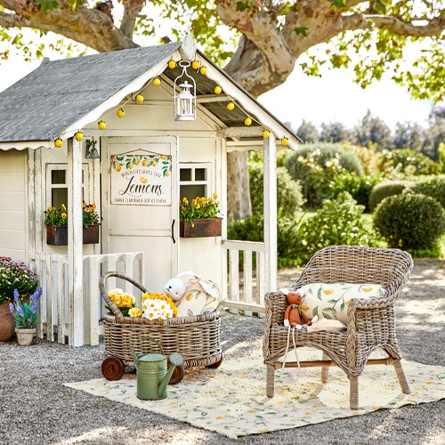 Vintage houten speelhuisje voor kinderen met rotan stoel en tuindecoraties buiten