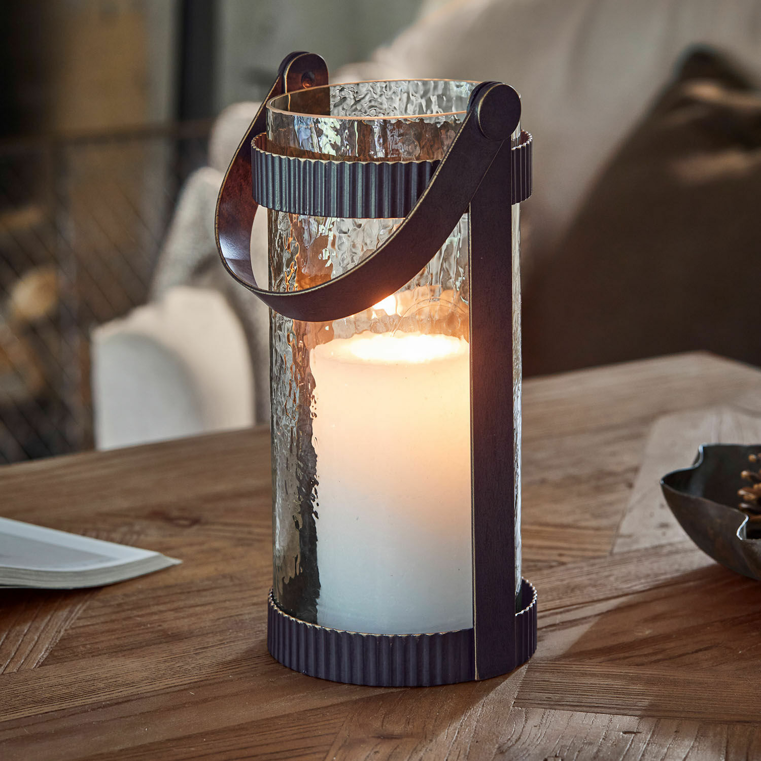 Lantaarn Uvelie Glazen lantaarn met witte kaars en zwart metalen handvat op houten tafel, sfeervolle woondecoratie