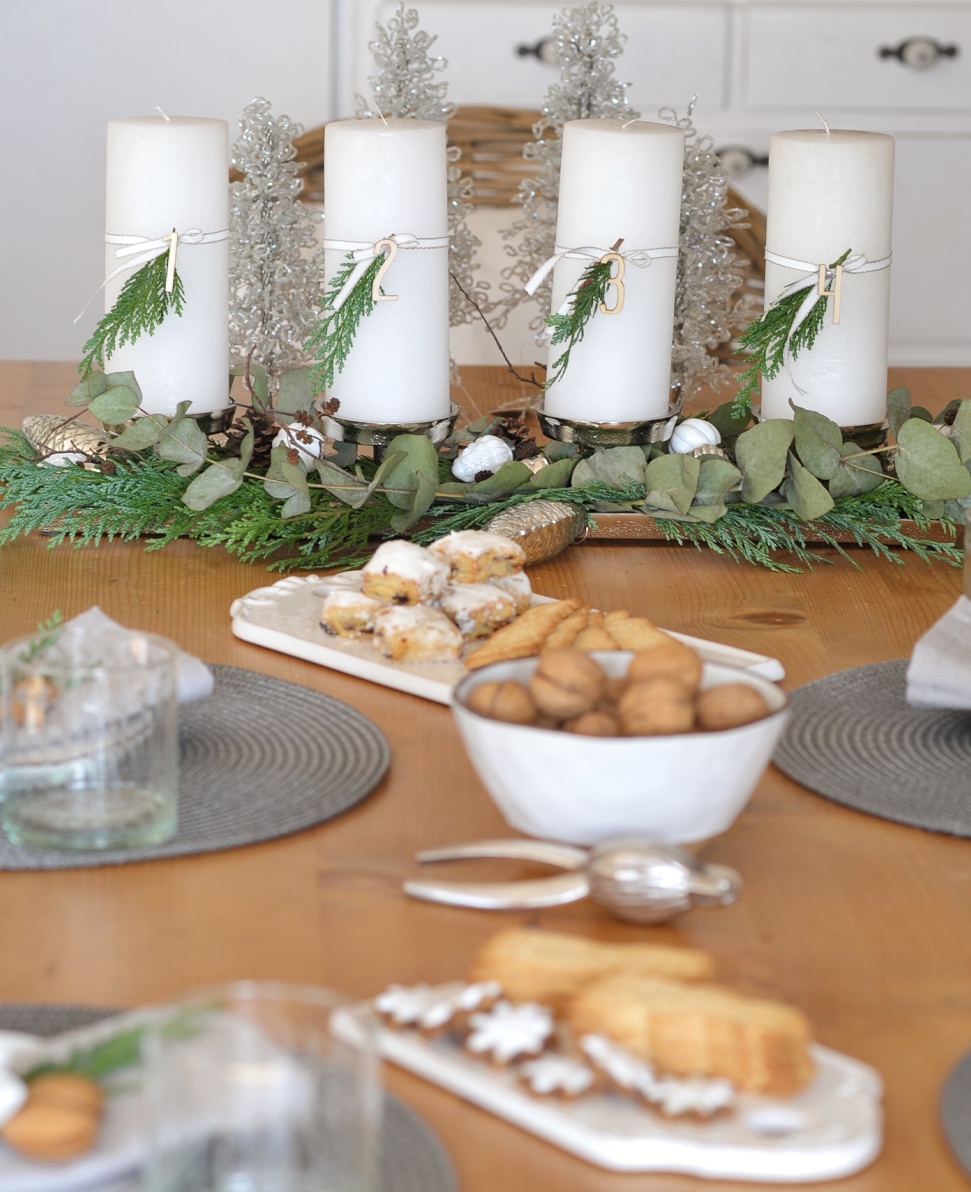 Witte adventskaarsen met groene takjes en houten cijfers op houten tafel met koekjes en noten