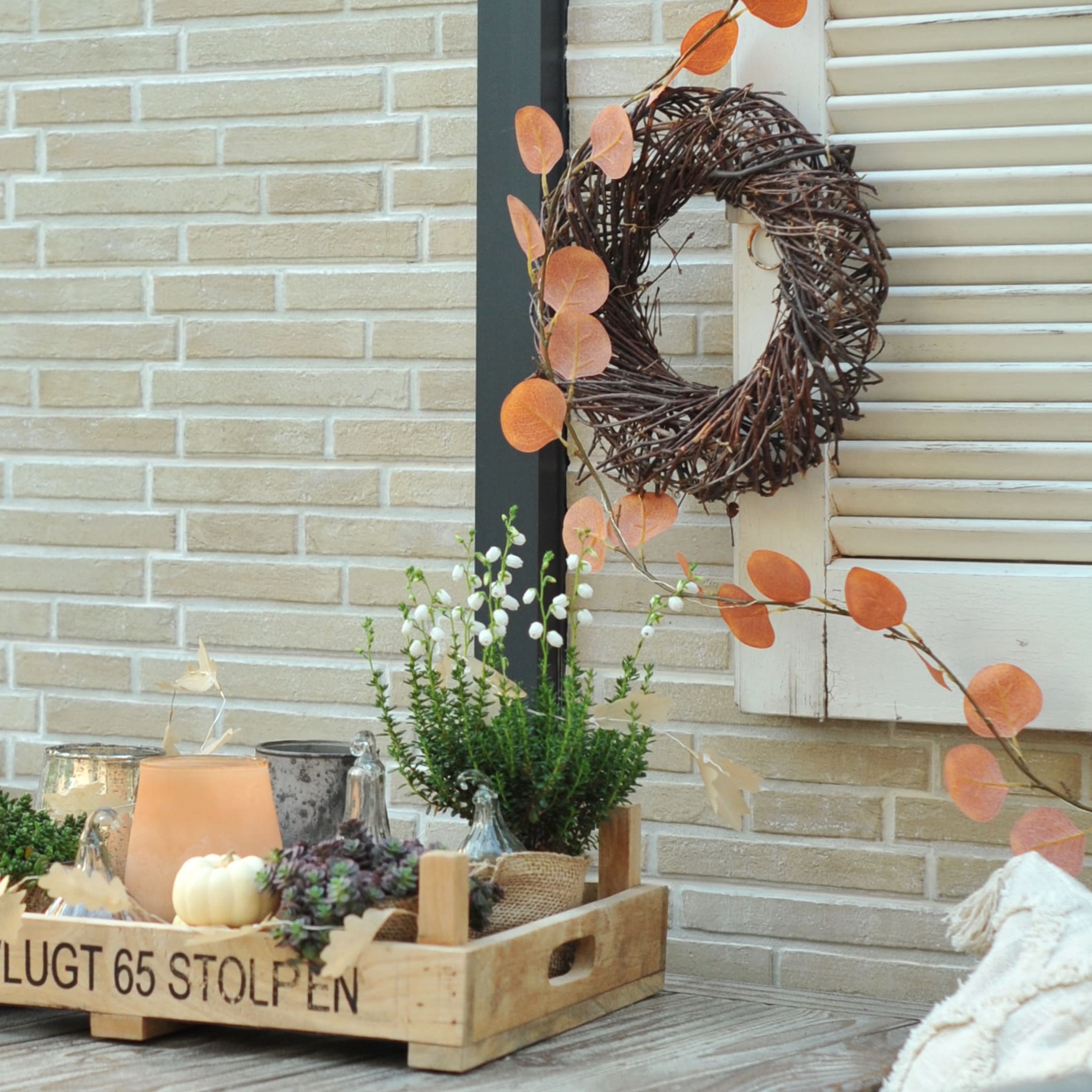 Houten dienblad met herfstdecoratie van planten, witte pompoen en kaarsen tegen bakstenen muur