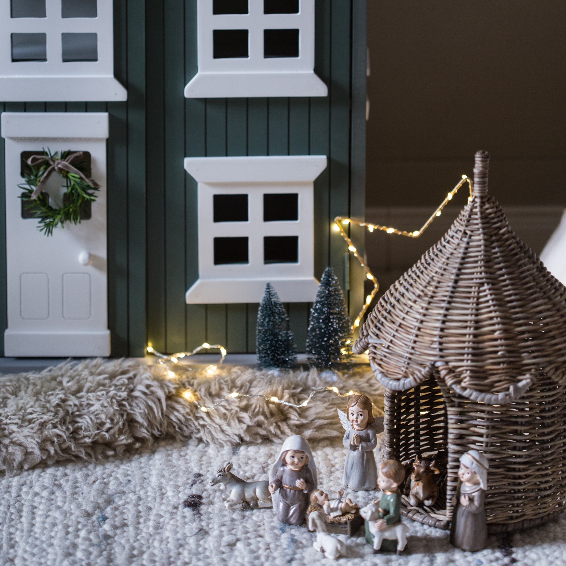 Kerstdecoratie met kerststalfiguren en rieten stal op tapijt met LED-lichtjes