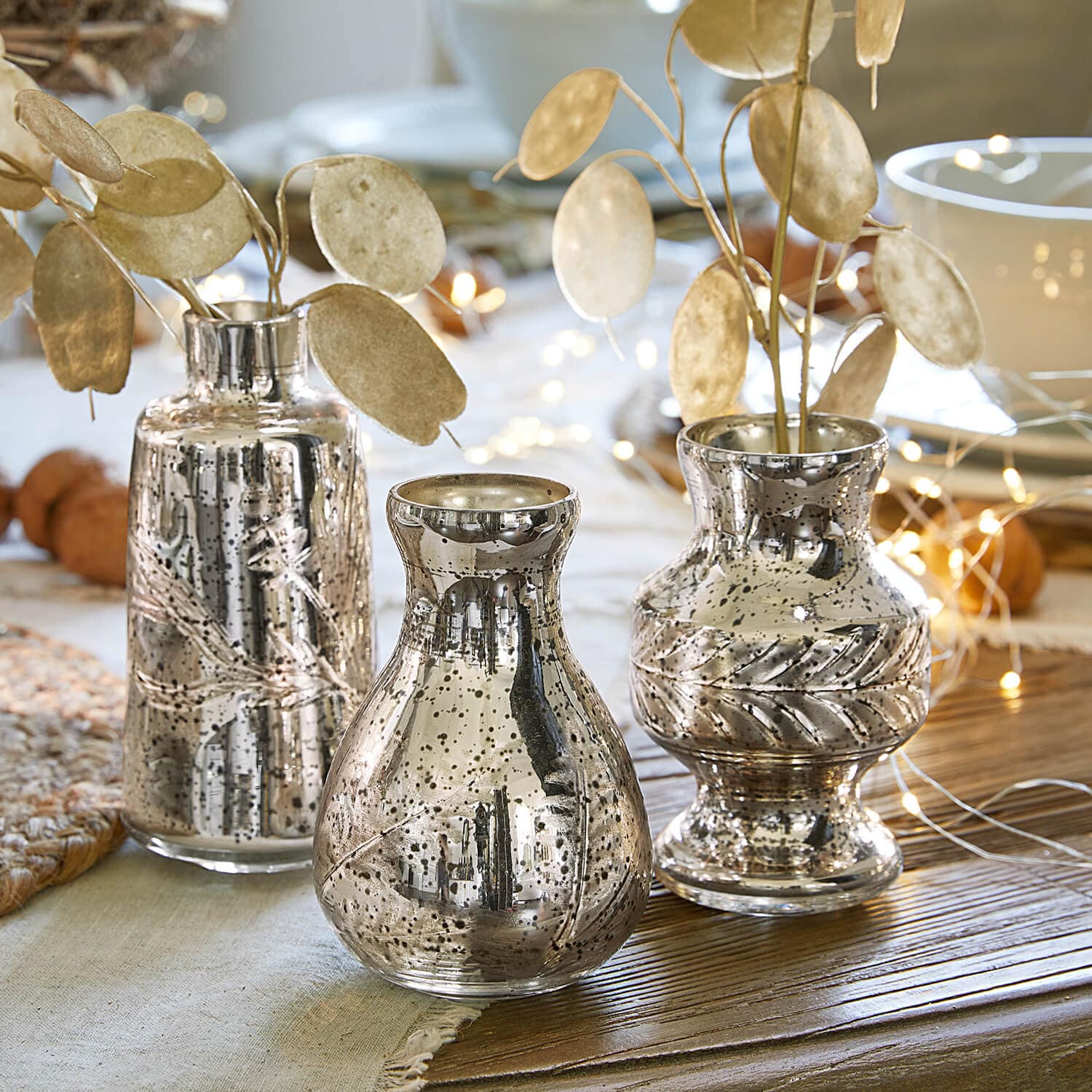 Set van drie zilverkleurige vazen met metallic glans en decoratieve bladeren op houten tafel