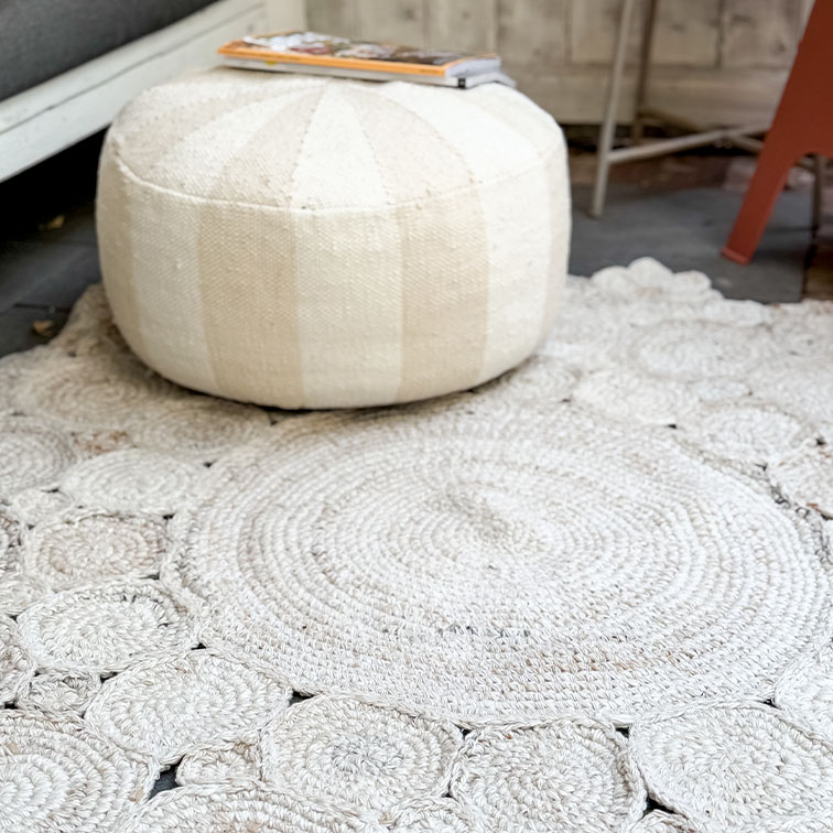 Ronde witte stoffen poef op lichte geweven vloerkleed, sfeervolle woondecoratie