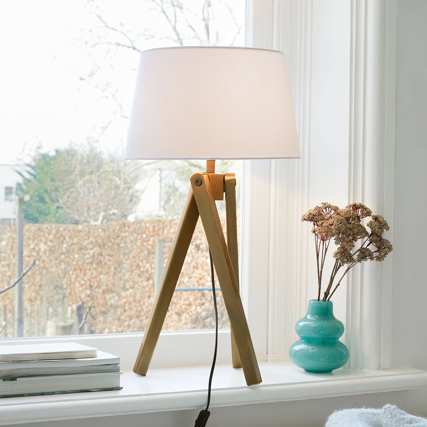 Tafellamp met houten voet en witte kap op vensterbank naast turquoise vaas