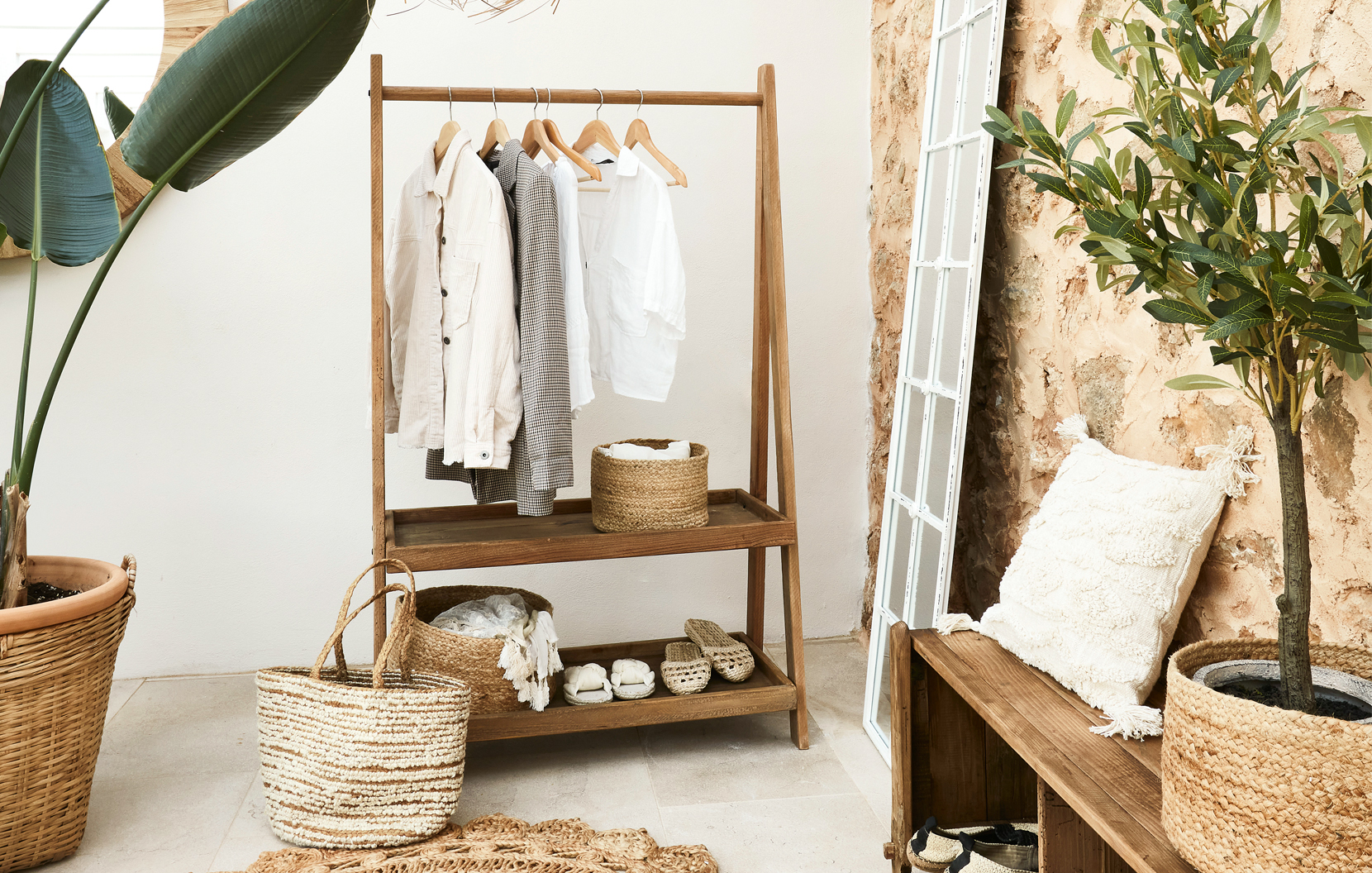 Houten kledingrek met lichte overhemden en rieten manden in boho interieur